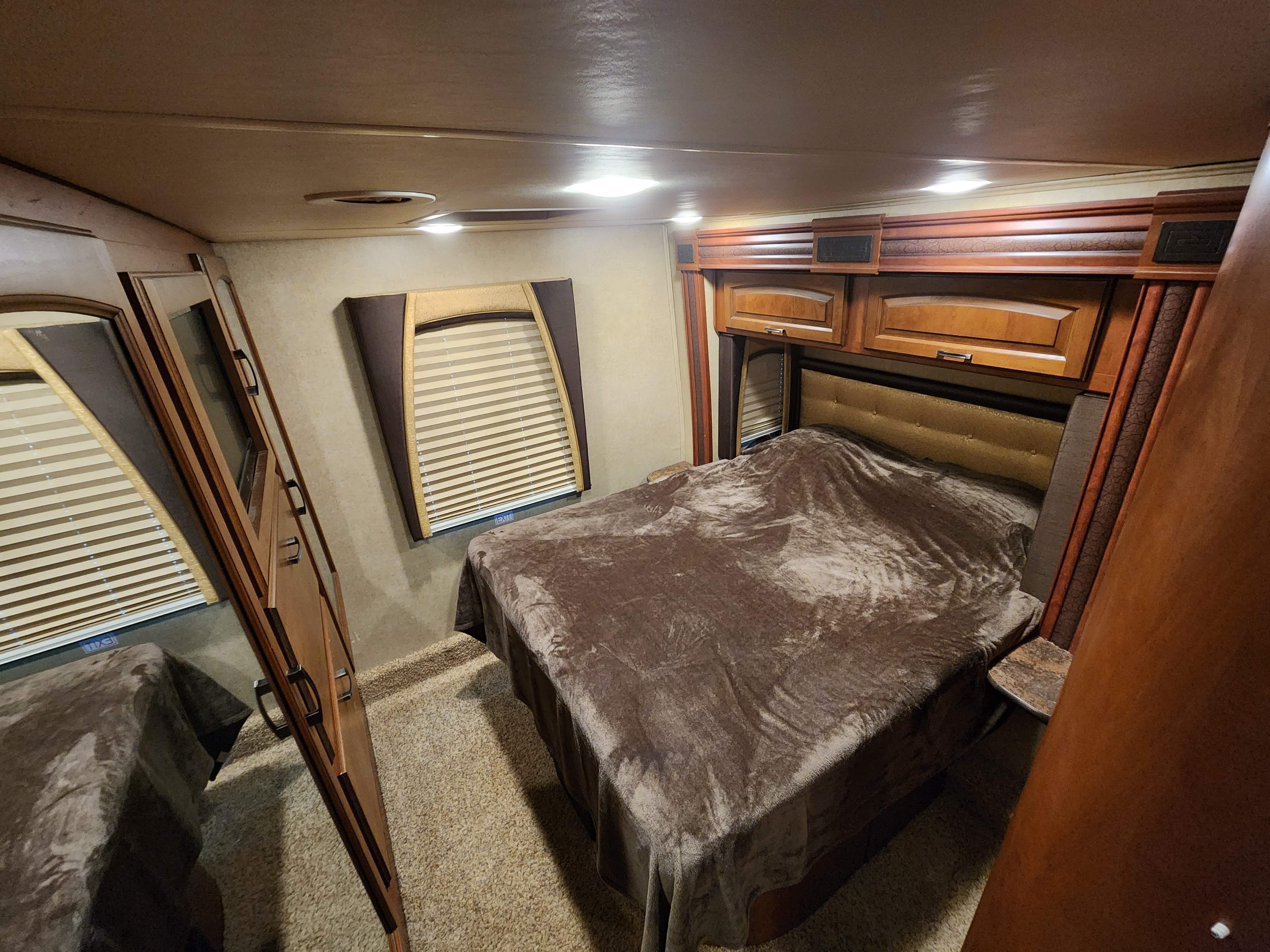 Comfortable RV rental bedroom with a large bed, overhead wood cabinets, and a window with blinds. Features a plush brown blanket.. Jayco Melbourne 2015