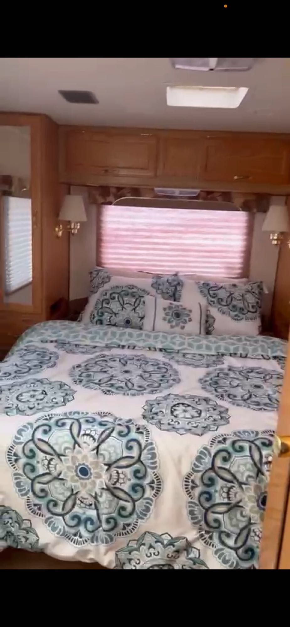 Comfortable RV rental bedroom with white and teal patterned bedding, overhead wood cabinets, and window blinds.. Gulf Stream Conquest 2000