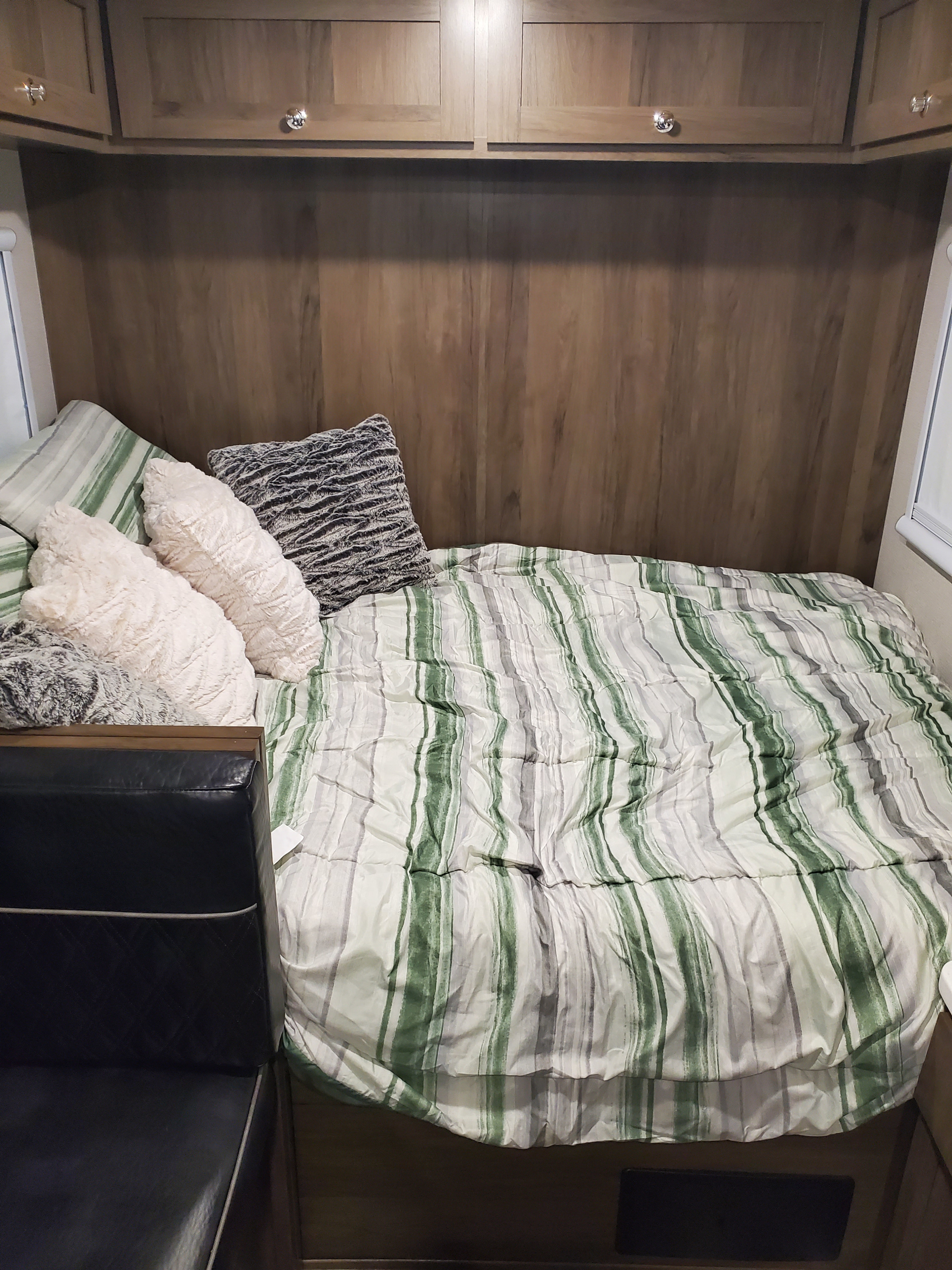 This cozy RV rental features a bed with striped comforter, plush pillows, and wooden overhead cabinets. Ideal camper interior.. Imperial Outdoors XploreRV 2023