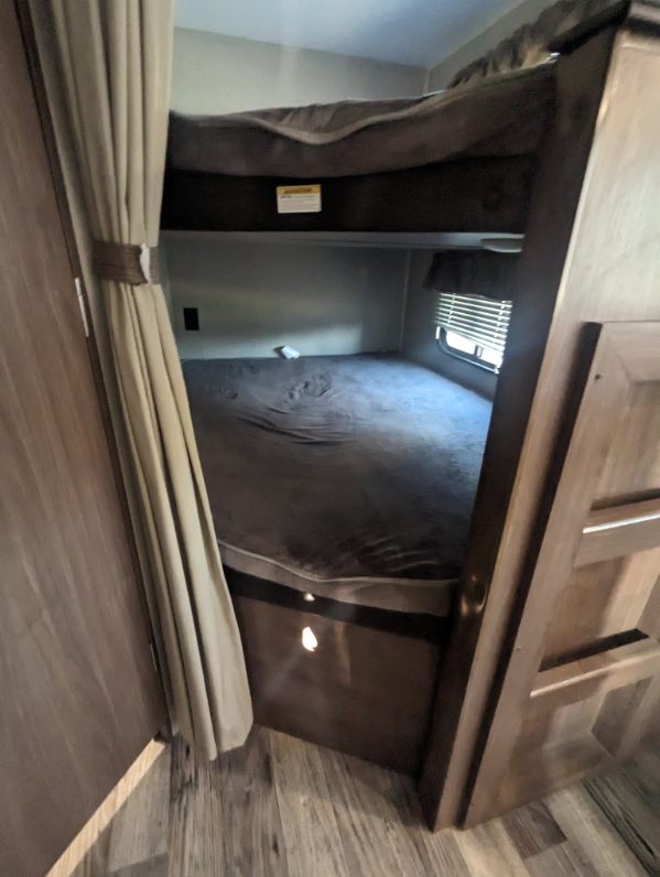 Cozy bunk beds in an RV rental, featuring curtains, a window with blinds, and wooden interior. Perfect for families.. Keystone RV Hideout LHS 2020