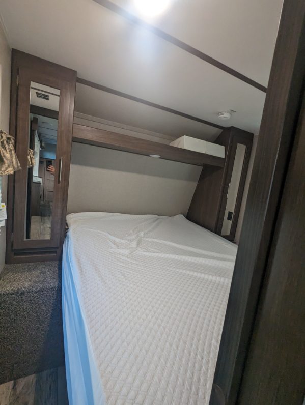 Inside an RV rental: a compact bedroom with a white bed, built-in storage, and mirror. Ready for your next travel adventure.. Keystone RV Hideout LHS 2020