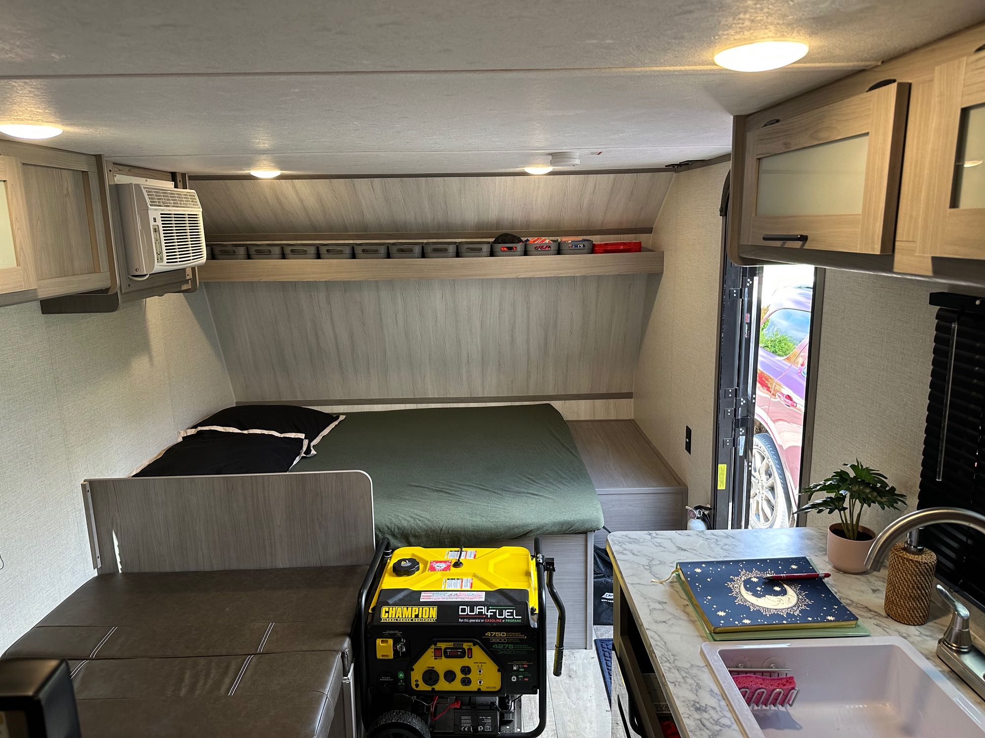 Inside an RV rental: a compact living space with bed, kitchen, AC, and a powerful Champion dual-fuel generator for your adventures.. Dutchmen Coleman Lantern LT 2023