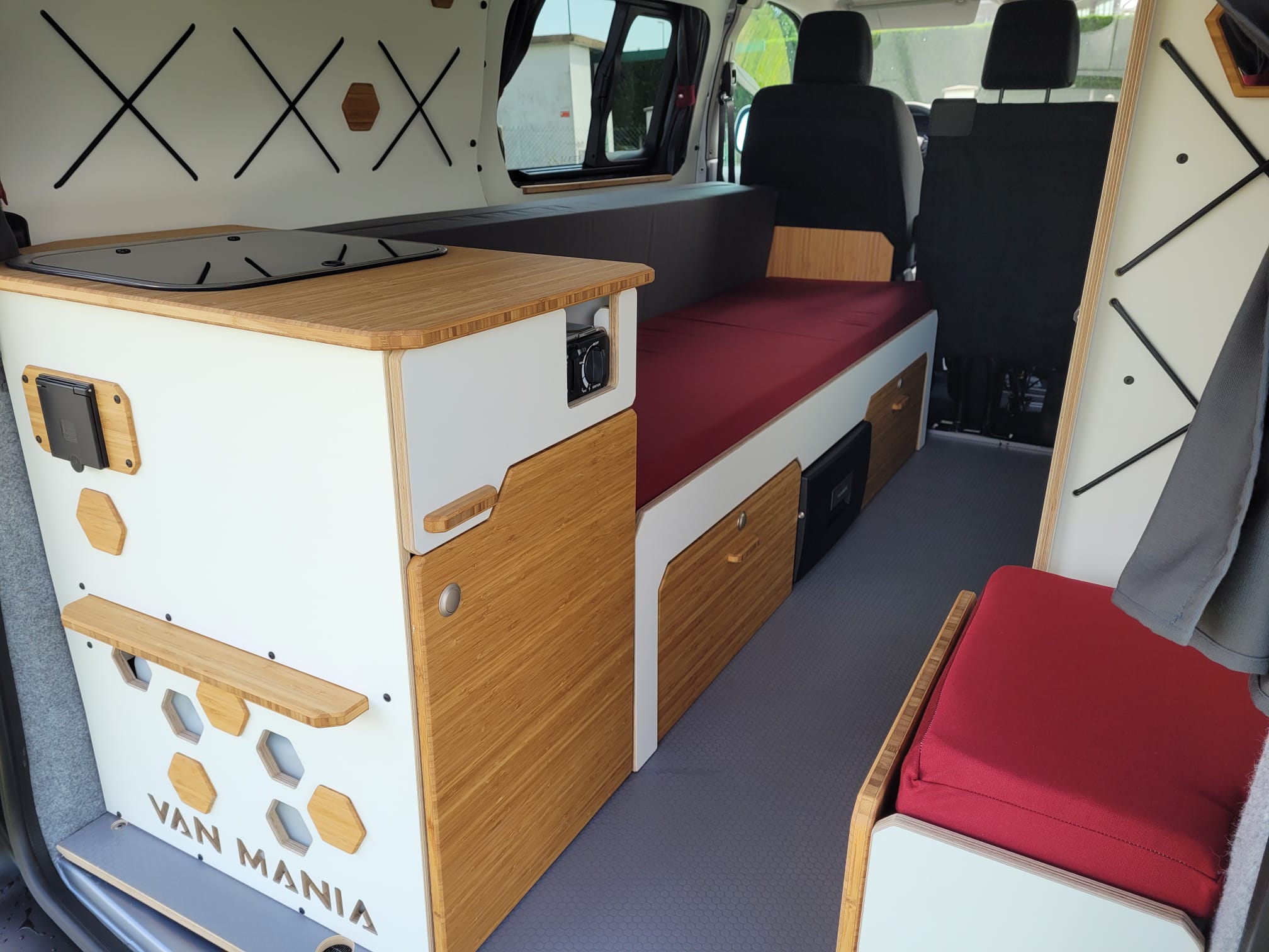 Interior of a stylish RV rental, featuring a bamboo kitchen counter, white cabinets, and red cushioned sleeping/seating areas.. Opel VIVARO 2025
