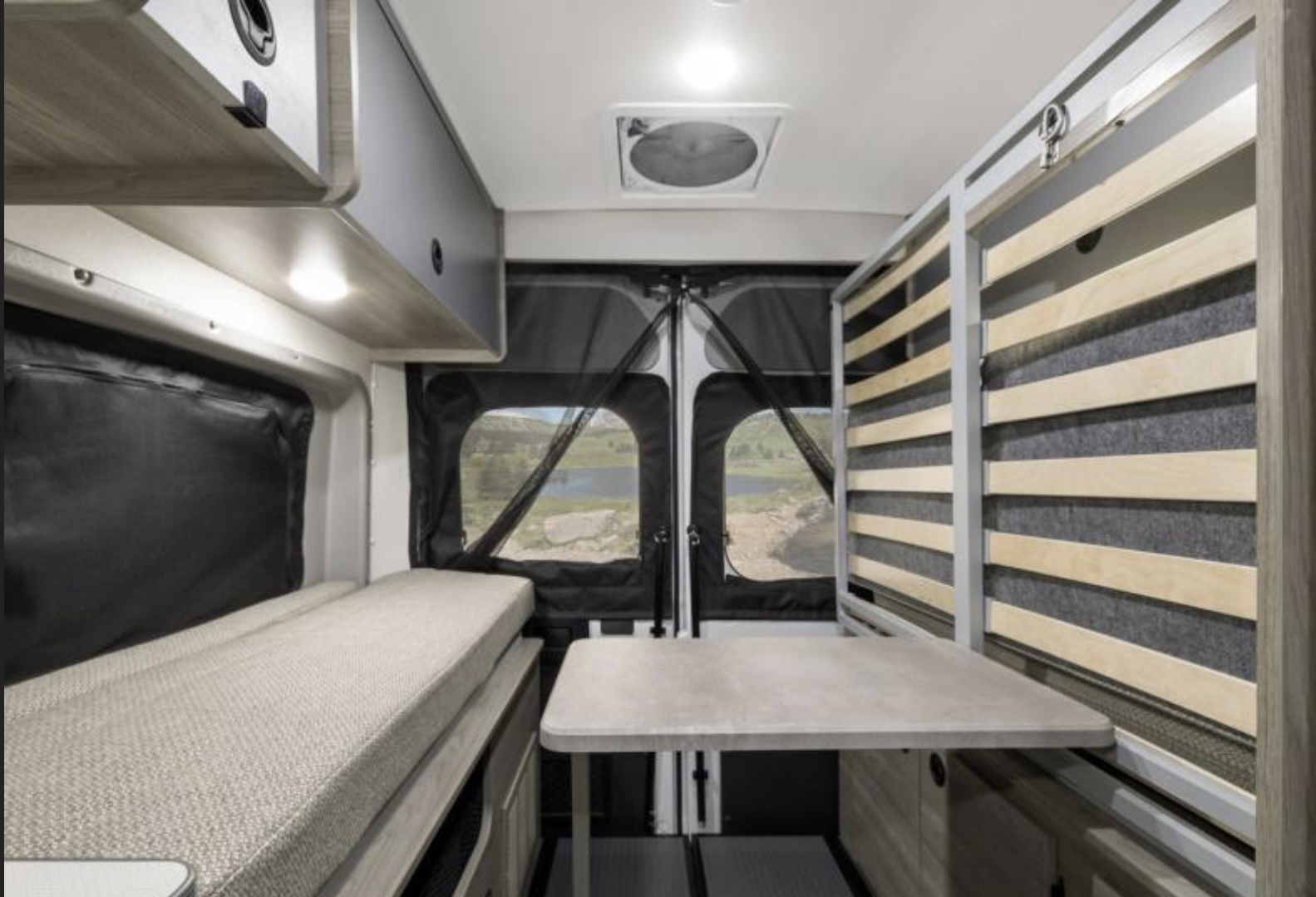 Inside a modern RV rental: a camper van's interior with a bench bed, table, storage, and beautiful lake view from the rear.. Winnebago Solis 2023