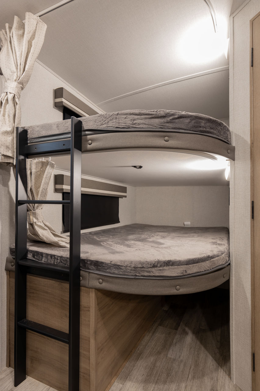 Cozy bunk beds in an RV rental, featuring a black ladder, soft grey mattresses, and privacy curtains.. Grand Design Imagine 2023