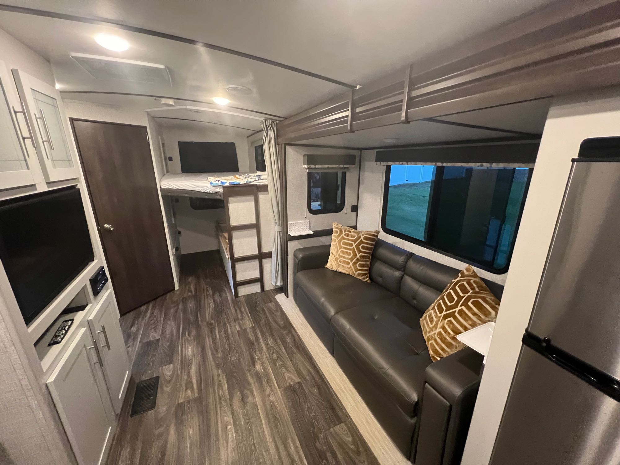 Inside this inviting RV rental: a modern living area with a dark sofa, bunk beds, and wood-look flooring.. Keystone RV Bullet Ultra Lite 2021