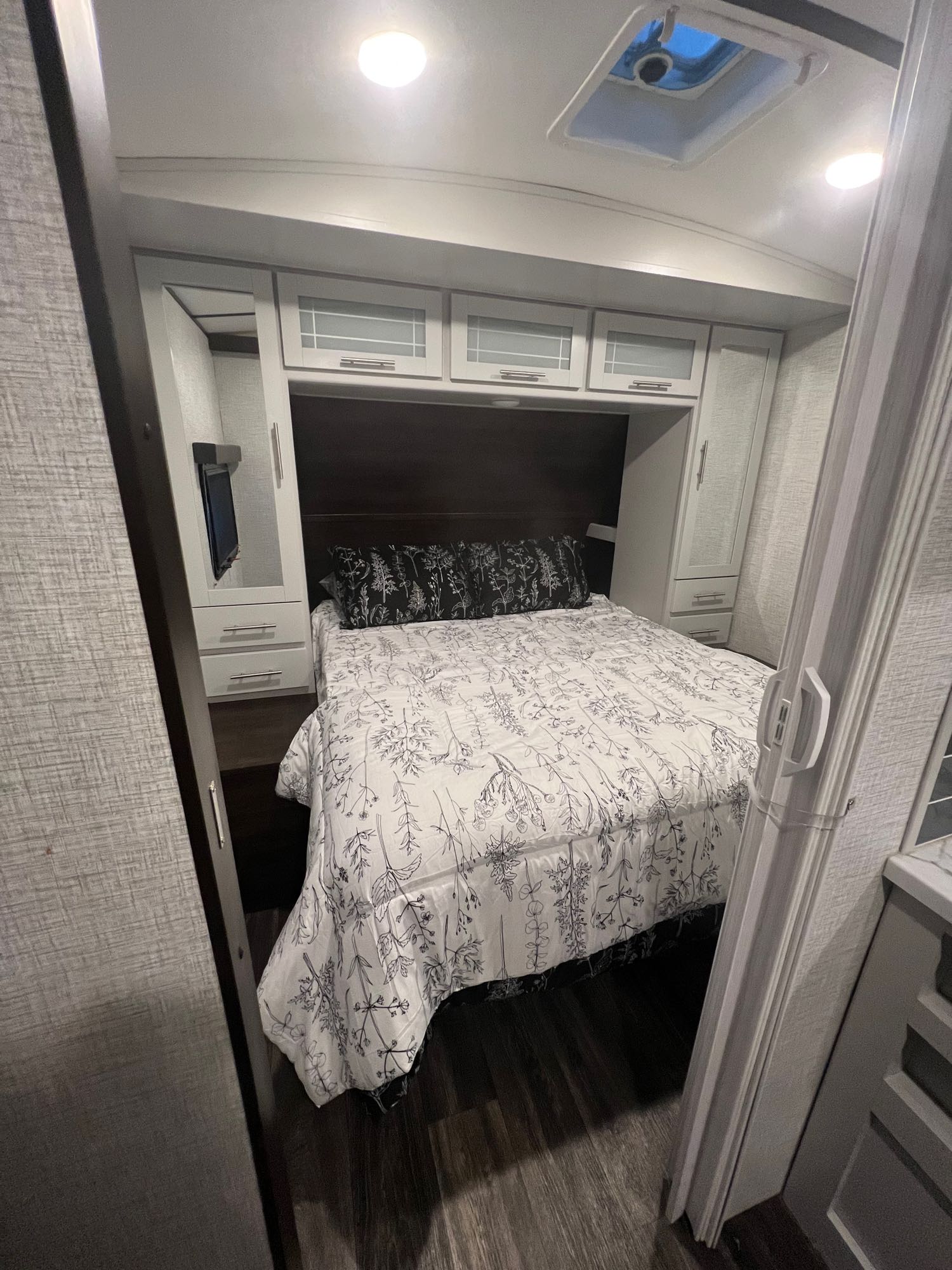Inside an RV rental bedroom: a bed with floral bedding, overhead cabinets, and wardrobes with a TV. Cozy and functional space.. Keystone RV Bullet Ultra Lite 2021