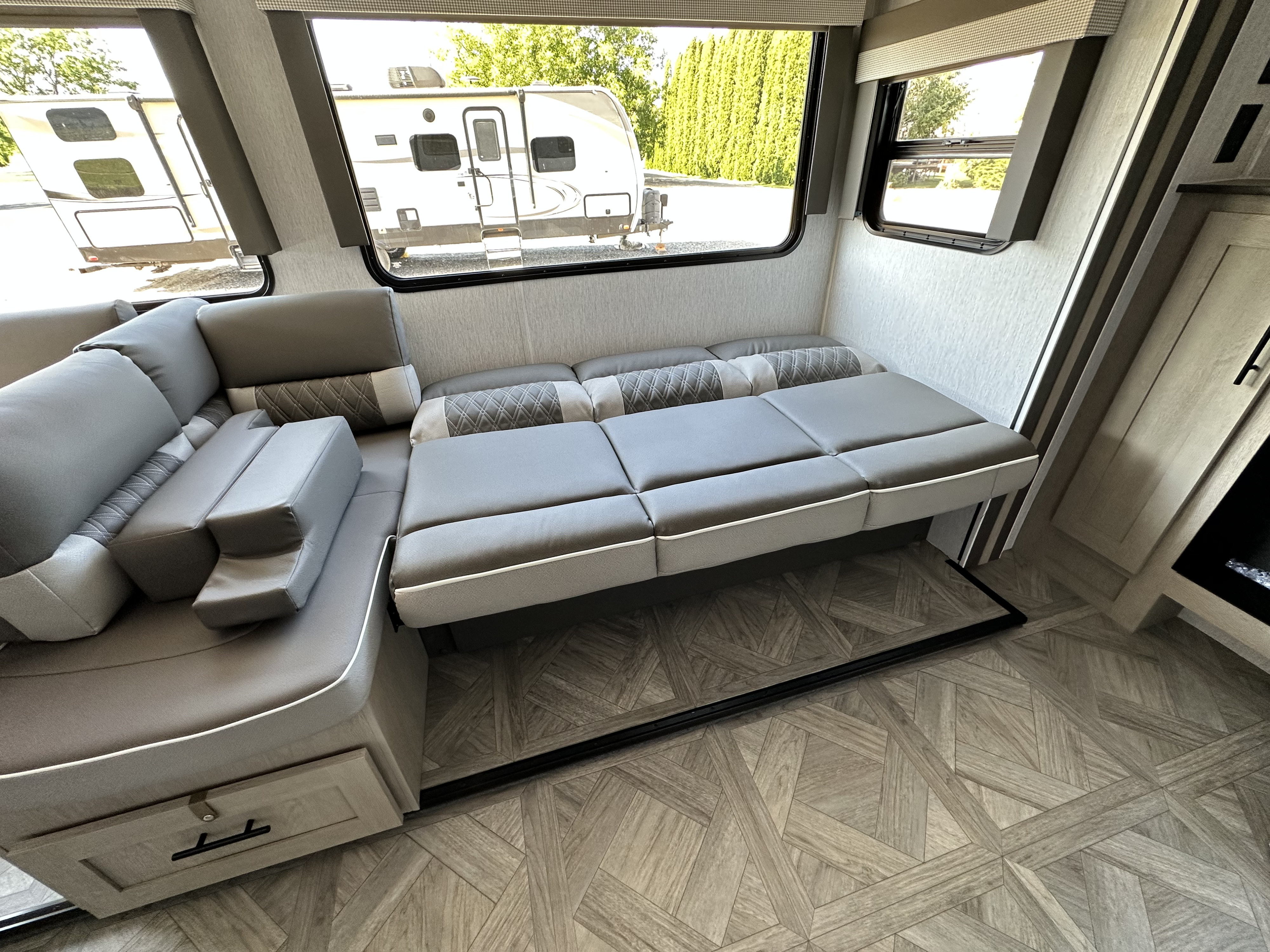 RV rental's inviting interior: gray convertible sofa bed, large windows showcasing parked campers, and modern floor.. Forest River Salem Cruise Lite 2023