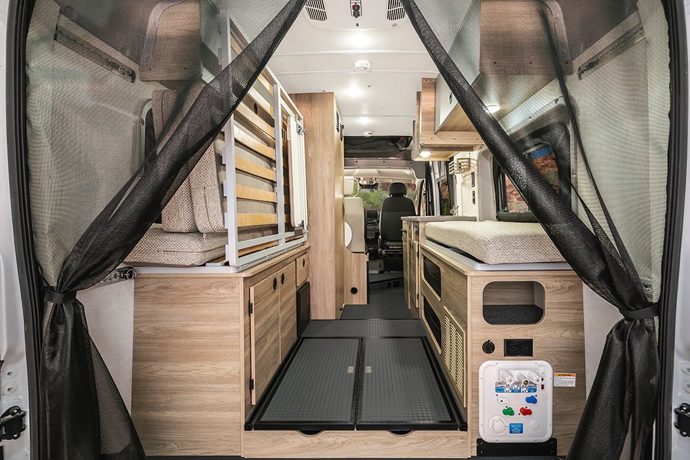This RV rental interior features a rear mesh screen, convertible bed, cabinetry, and a visible utility panel.. Winnebago Solis 2023