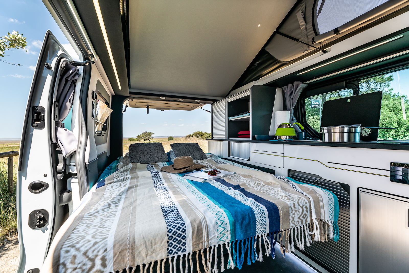 Comfortable campervan interior with bed, kitchen, and nature views. Perfect for an RV rental adventure.. HANROAD TREK 4 2023