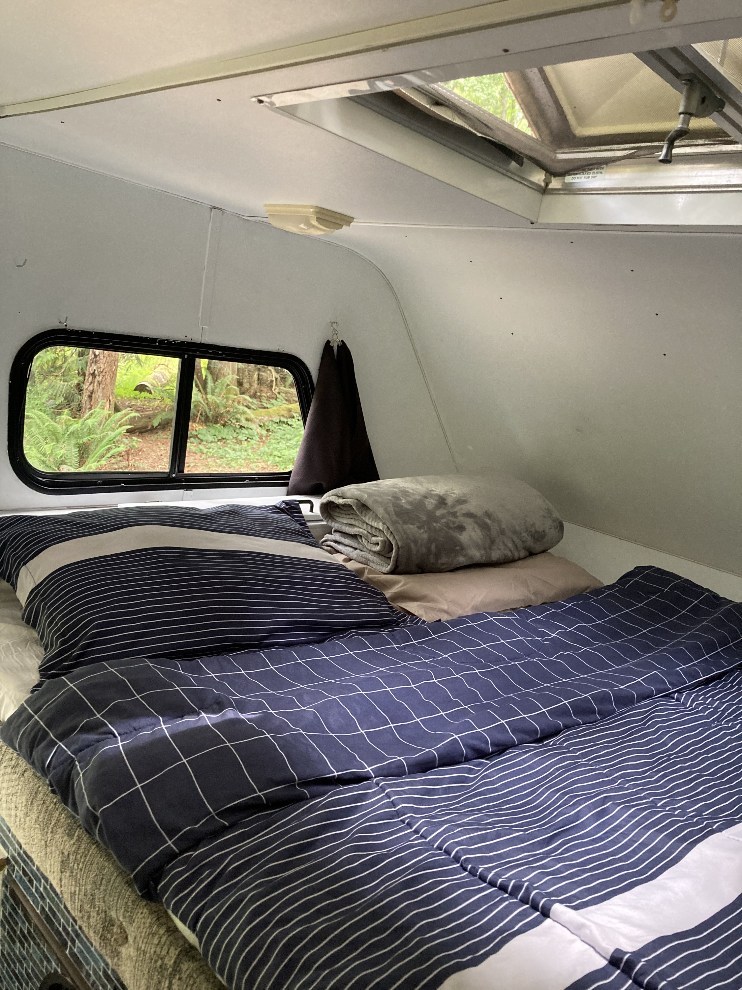 Cozy RV rental bedroom with a forest view, featuring striped bedding and an open skylight. Perfect for a peaceful getaway!. Gmc Other 2003