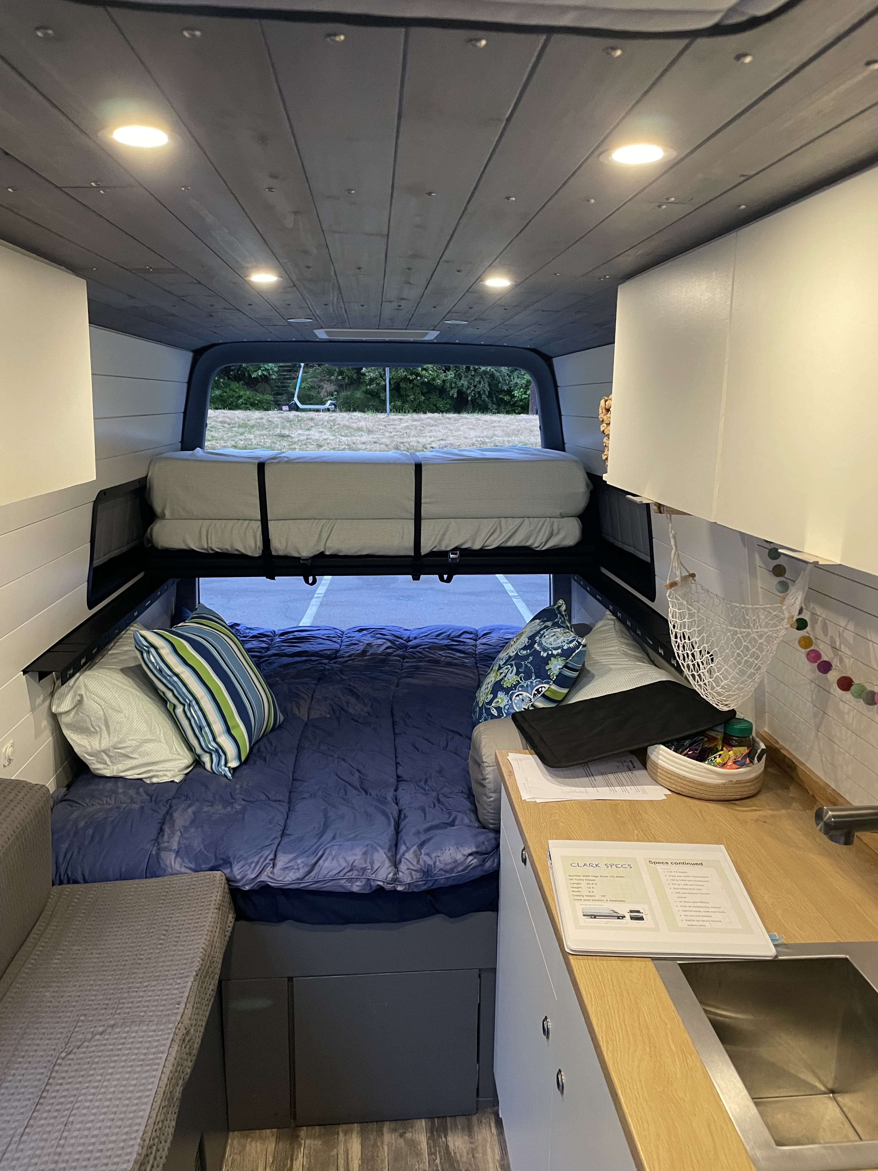 Interior view of an RV rental showcasing a cozy two-level bed system, kitchenette, and bright ceiling lights.. Mercedes-Benz Sprinter 2018