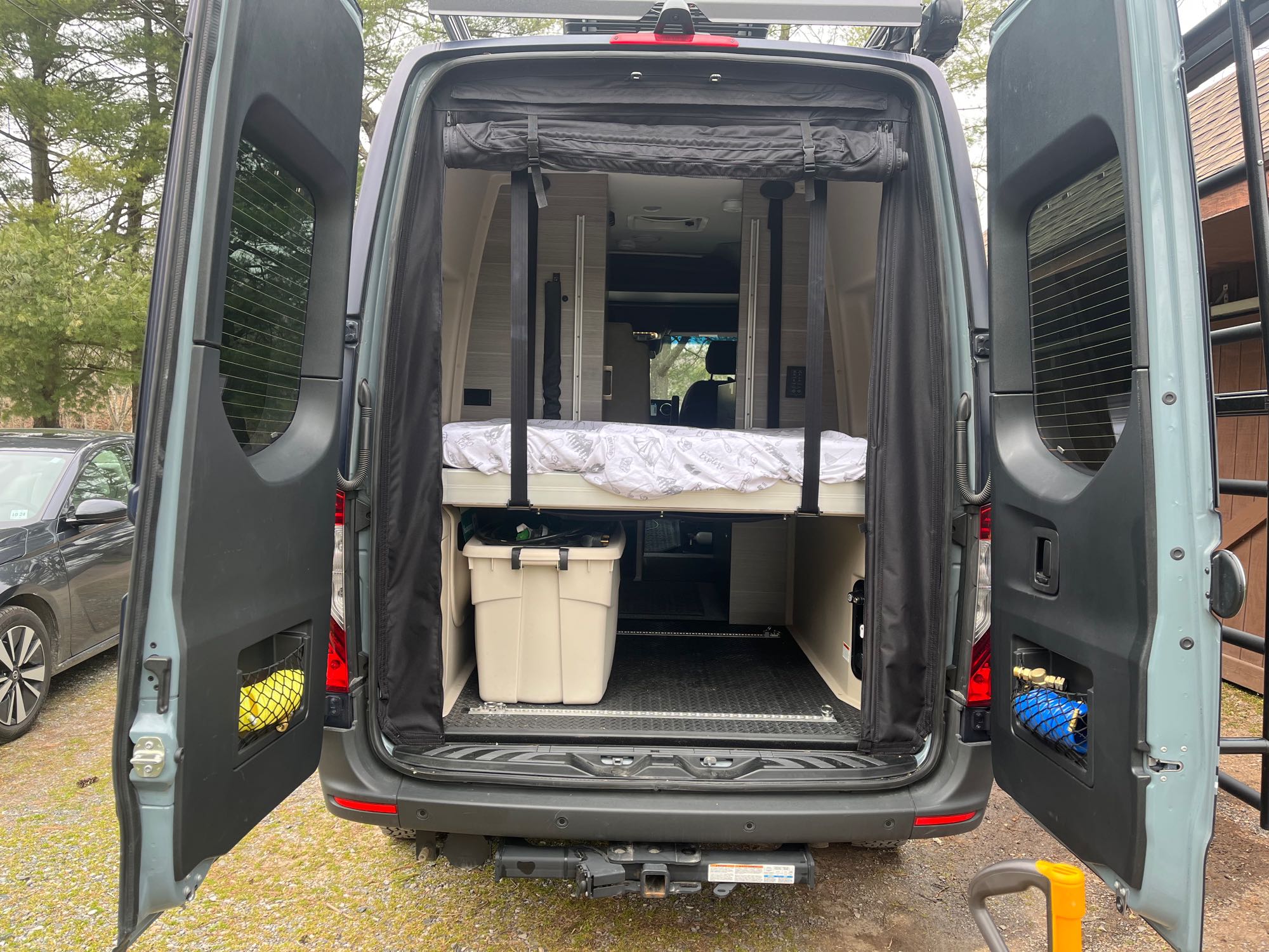 Rear view of a gray RV rental with doors open, revealing a bed & storage. A ladder is seen on the right door. Ideal for mobile living.. JAYCO TERRAIN 19Y 2023