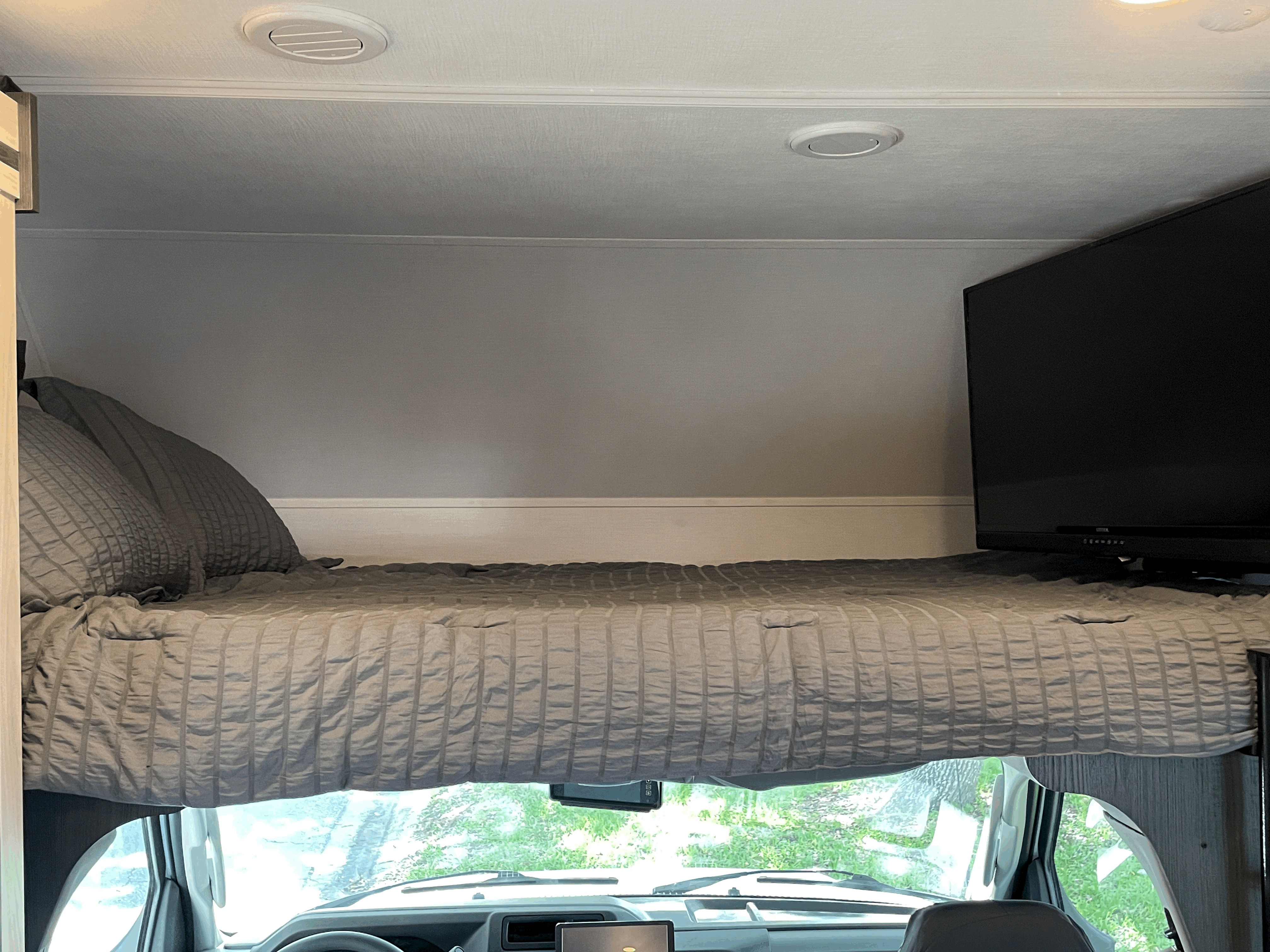 Cozy over-cab sleeping area in an RV rental, complete with a TV and view from the windshield. Ideal for adventurous travels.. Forester LE 2023