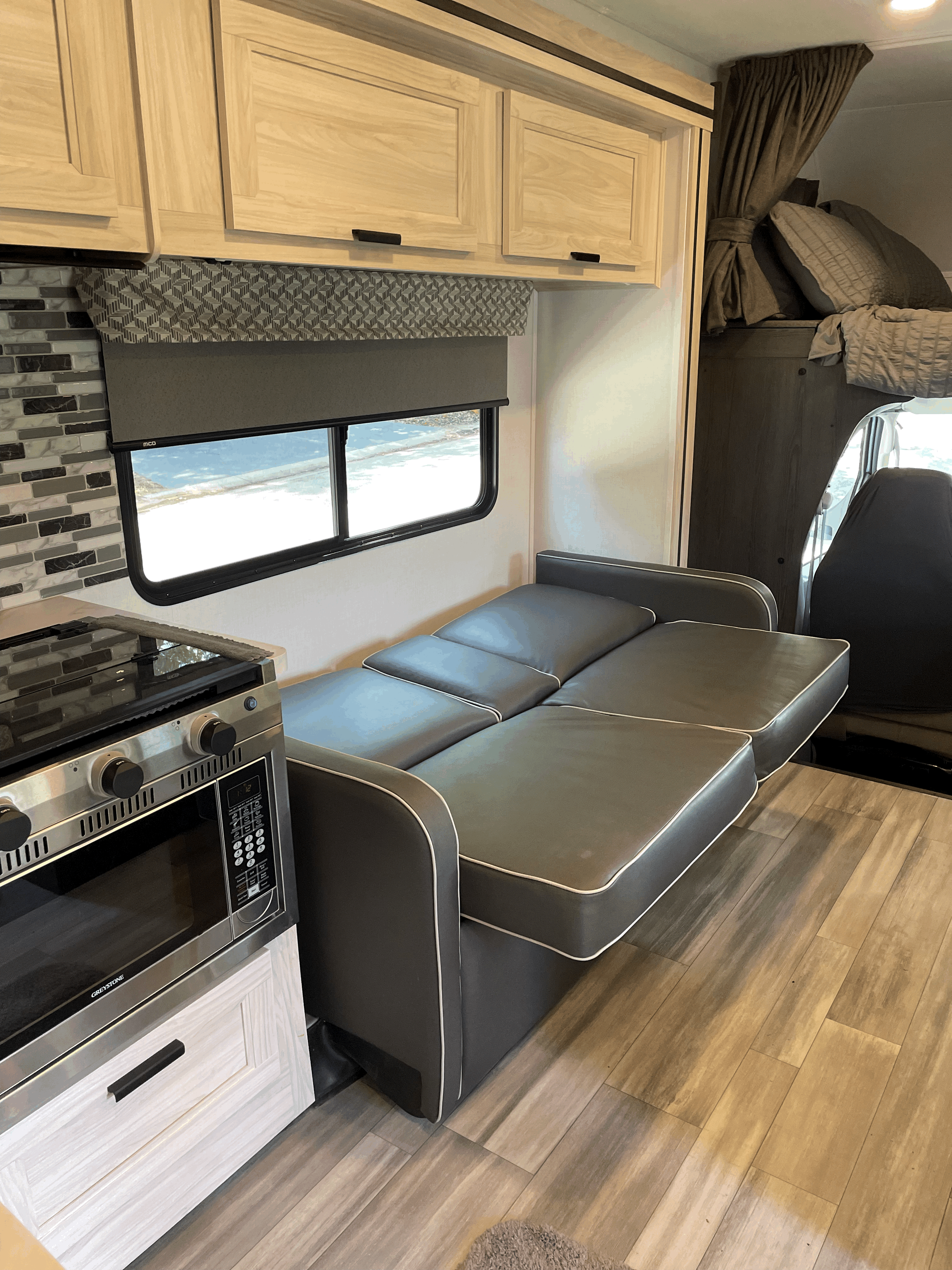 Inside an RV rental: sofa/bed extended, compact kitchen with oven and cabinets, plus a window view.. Forester LE 2023