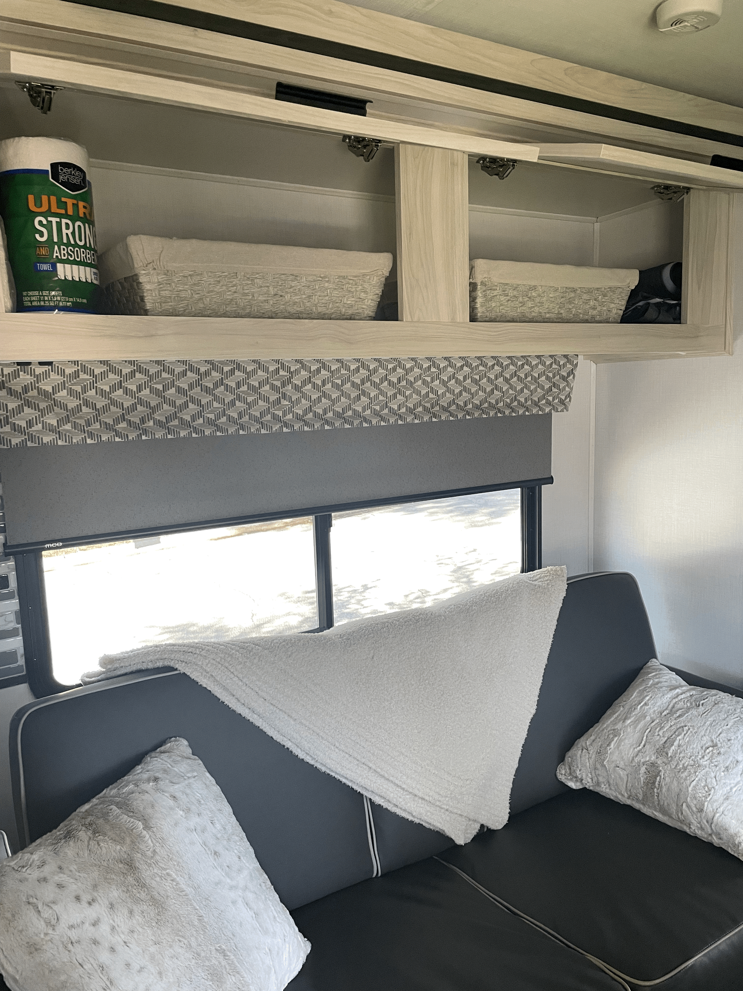 RV rental interior: organized overhead storage, cozy sofa with pillows, and a bright window, enhancing travel comfort.. Forester LE 2023