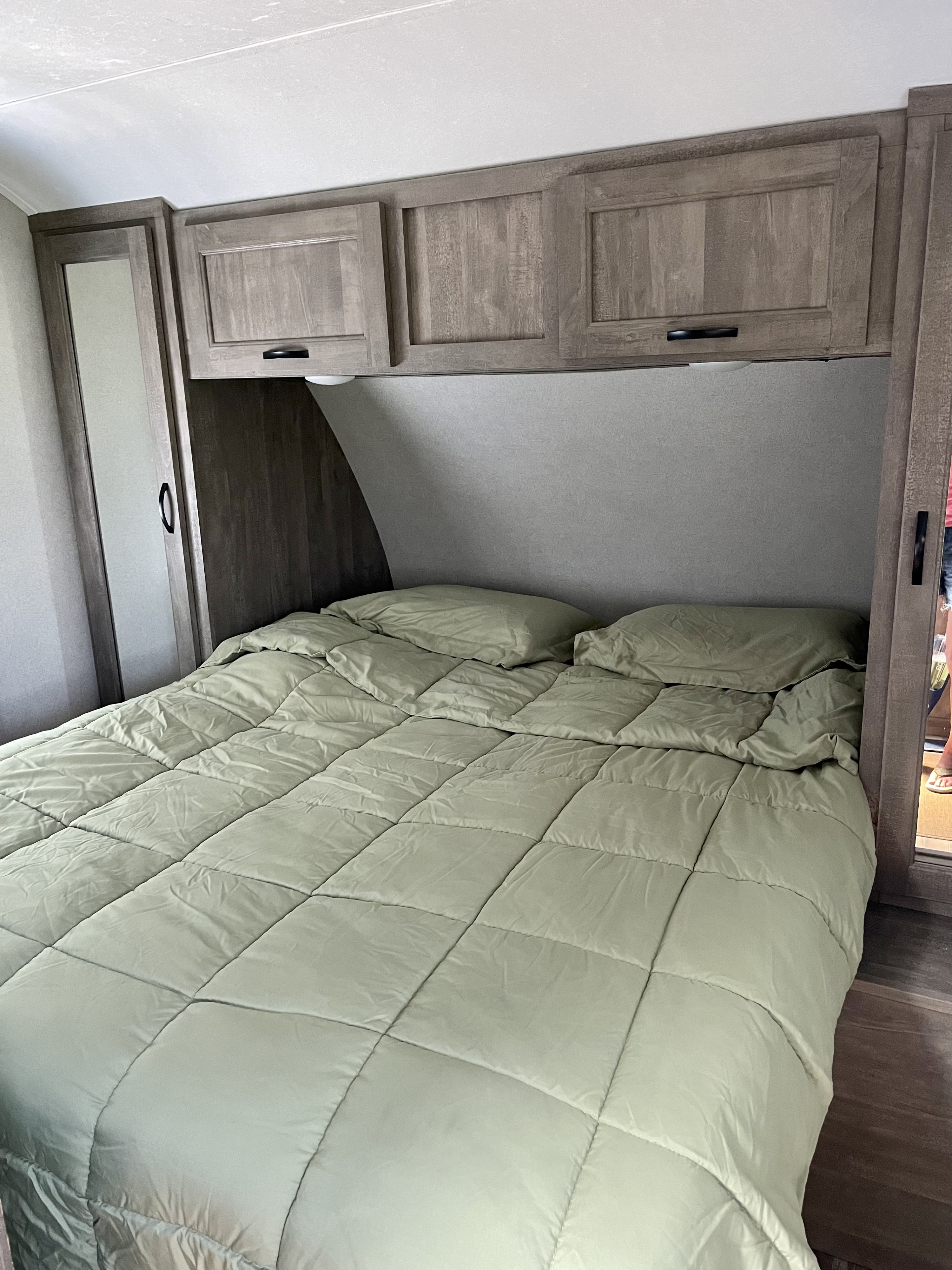 RV rental bedroom featuring a comfy bed with light green comforter, ample overhead storage, and wardrobes.. Forest River Vibe 2020
