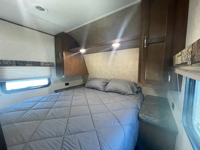 Inside this RV rental: a cozy bedroom featuring a grey bed, overhead cabinets, and a window for natural light.. Jayco Jay Flight SLX 2017