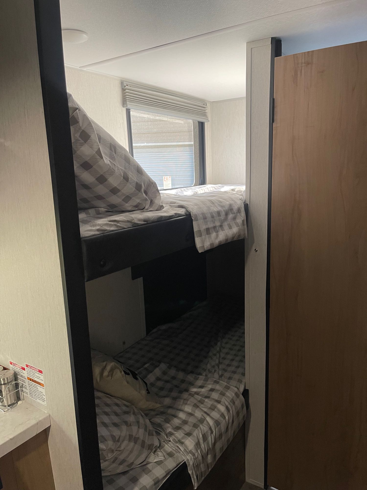 RV rental interior showcasing cozy bunk beds with checkered bedding and a window. A compact and practical sleeping space.. Forest River Cherokee Wolf Pup 2023