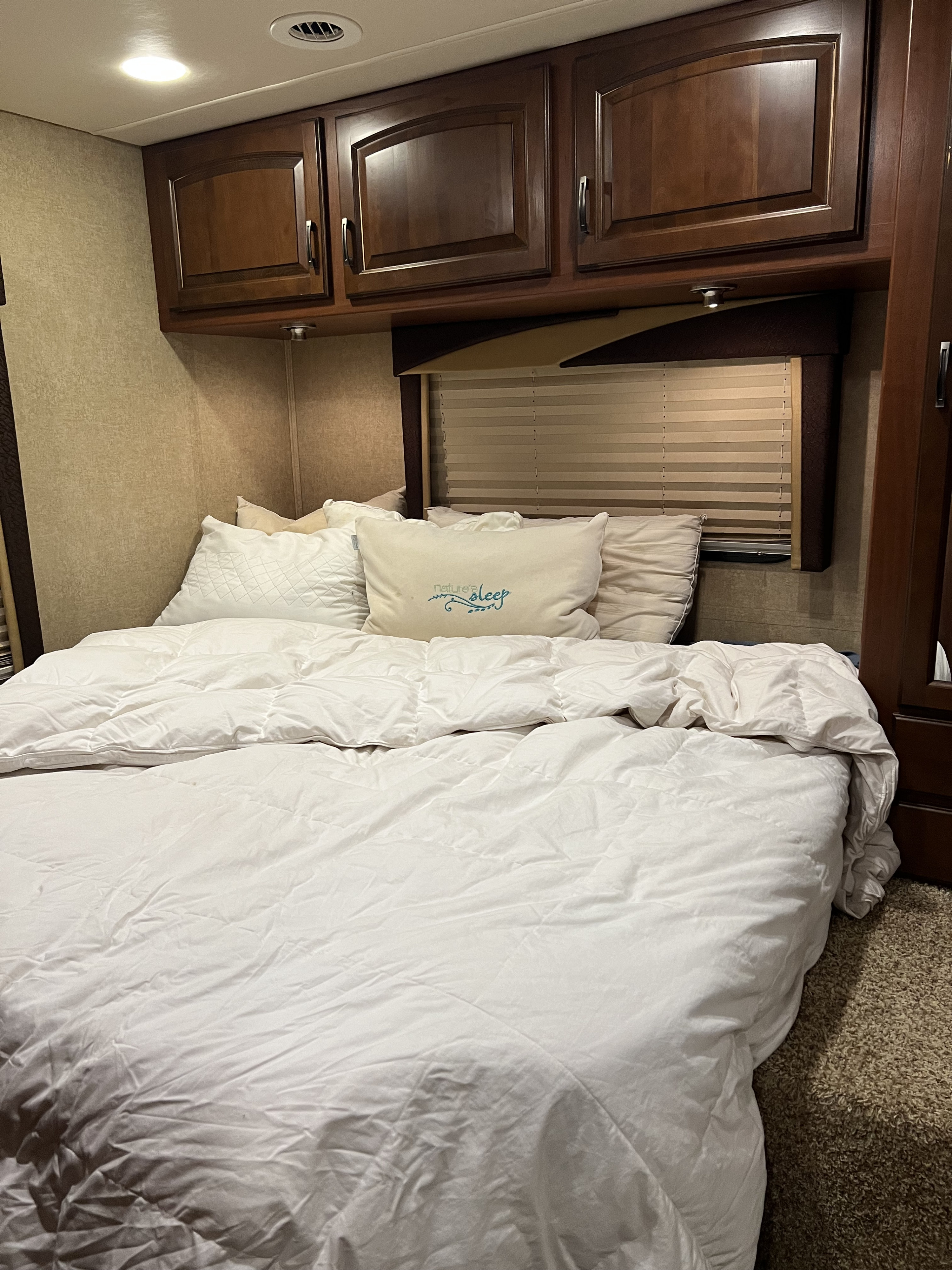 Cozy RV rental bedroom with white bedding, overhead cabinets, and window blinds.. Jayco Greyhawk 2015