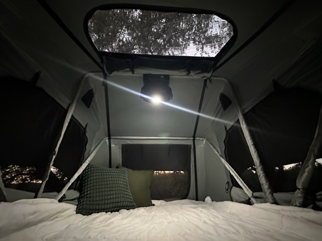 Cozy RV rental tent interior with bed, pillows, and bright overhead light for a comfortable night.. Sunset Park RV SunRay 2023