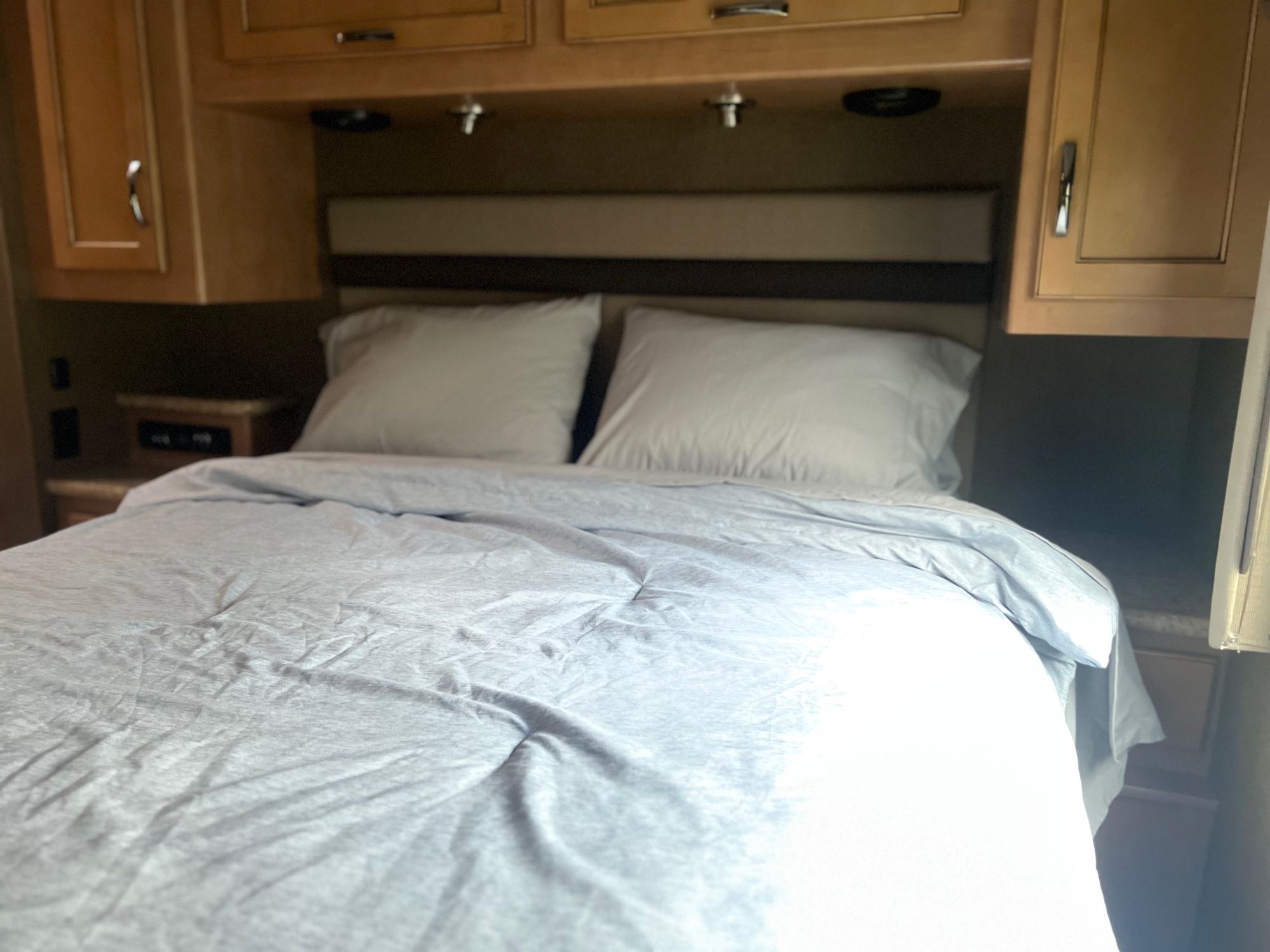 Cozy RV rental bedroom with a comfy bed, white pillows, and wooden overhead cabinets for a comfortable stay on the road.. Thor A.C.E. 2016