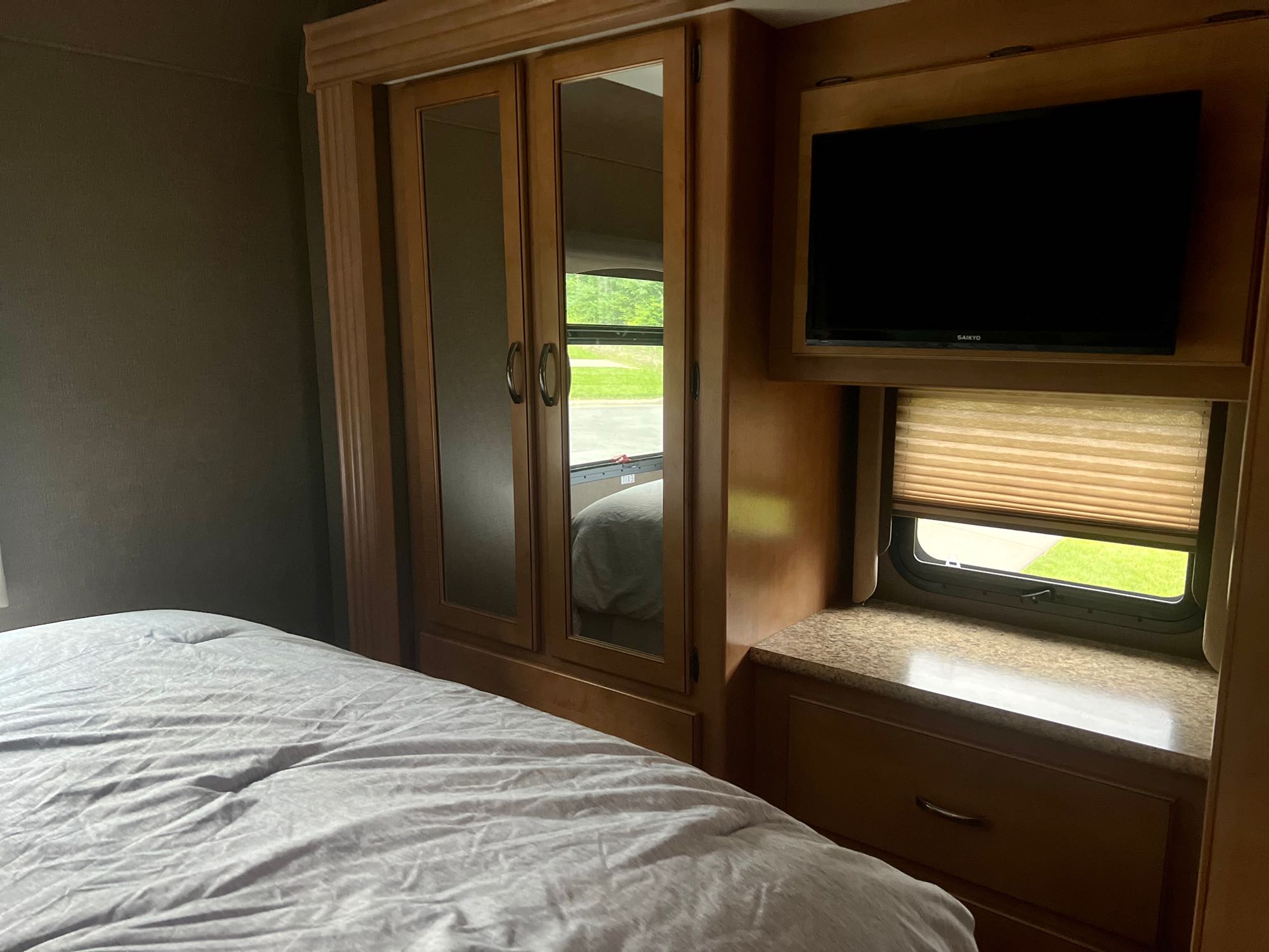 Cozy RV rental bedroom features a comfy bed, mirrored wardrobe, TV, and window with blinds. Ideal travel comfort!. Thor A.C.E. 2016
