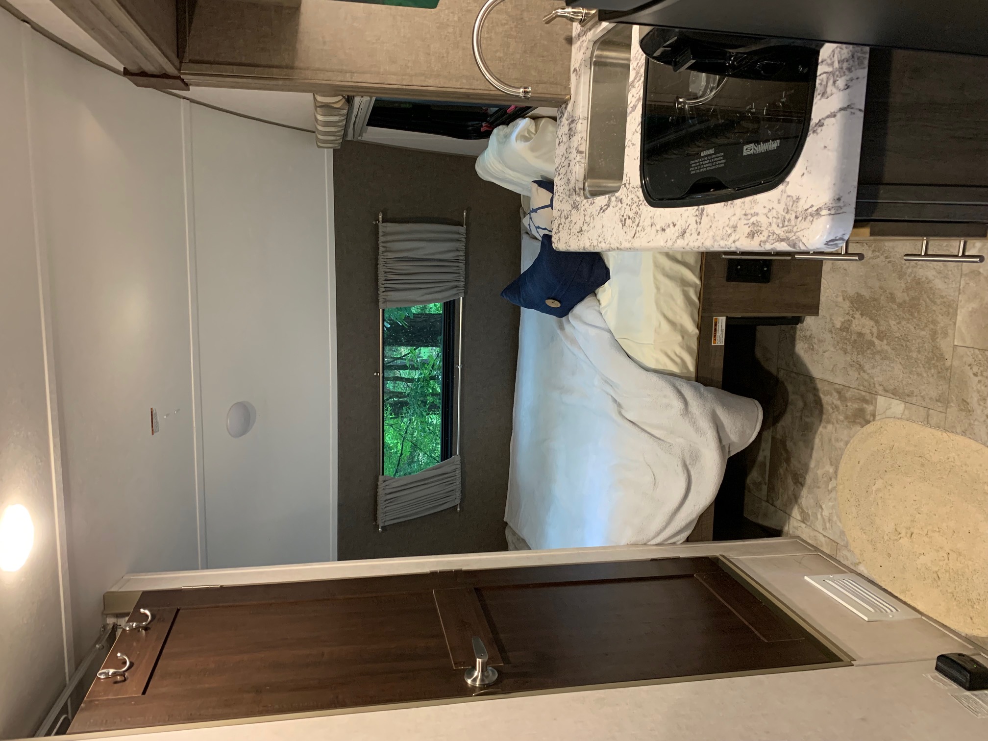 RV rental interior: cozy bedroom area, compact kitchen with sink/stovetop, and window looking out at trees.. Forest River R-Pod 2017