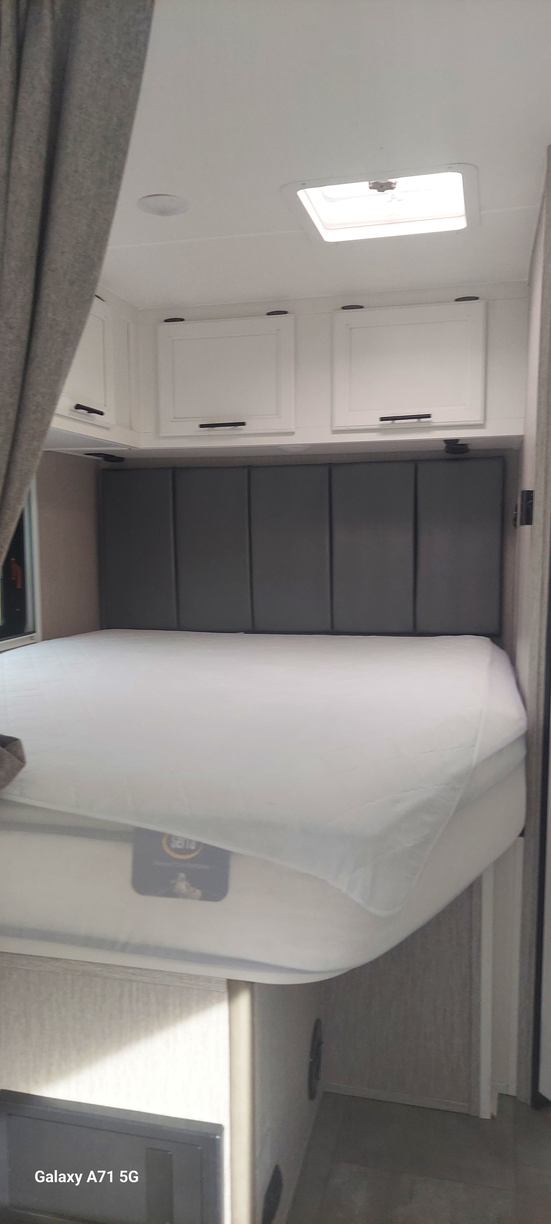 RV rental bedroom: A comfortable bed with a white mattress cover, gray padded headboard, and white overhead cabinets.. Forest River Coachmen Cross Trail XL 2022