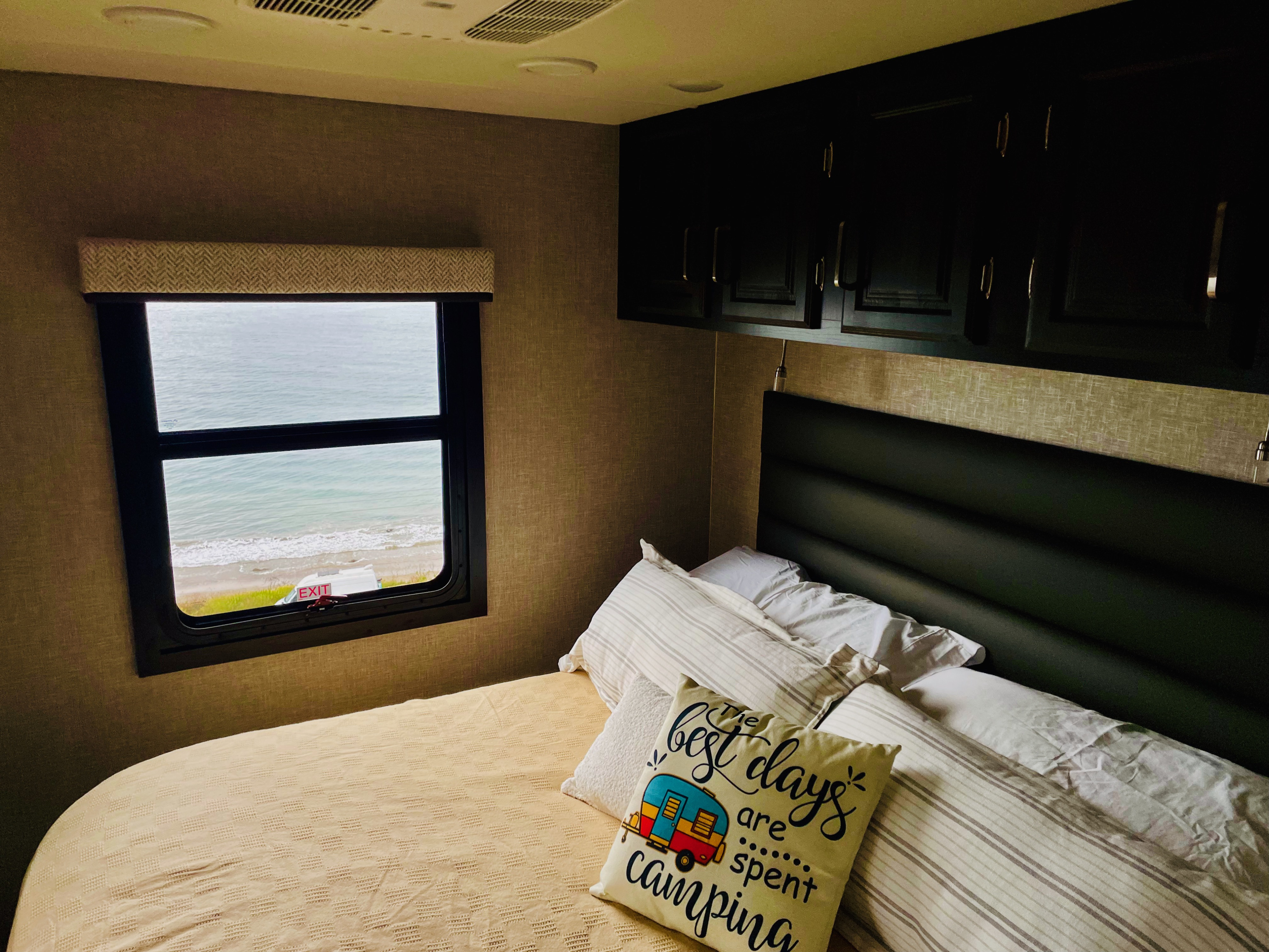 Experience an RV rental! Relax in this cozy RV bedroom, with a comfy bed, camping pillow, and ocean view from the window.. Entegra Coach Vision XL 2023