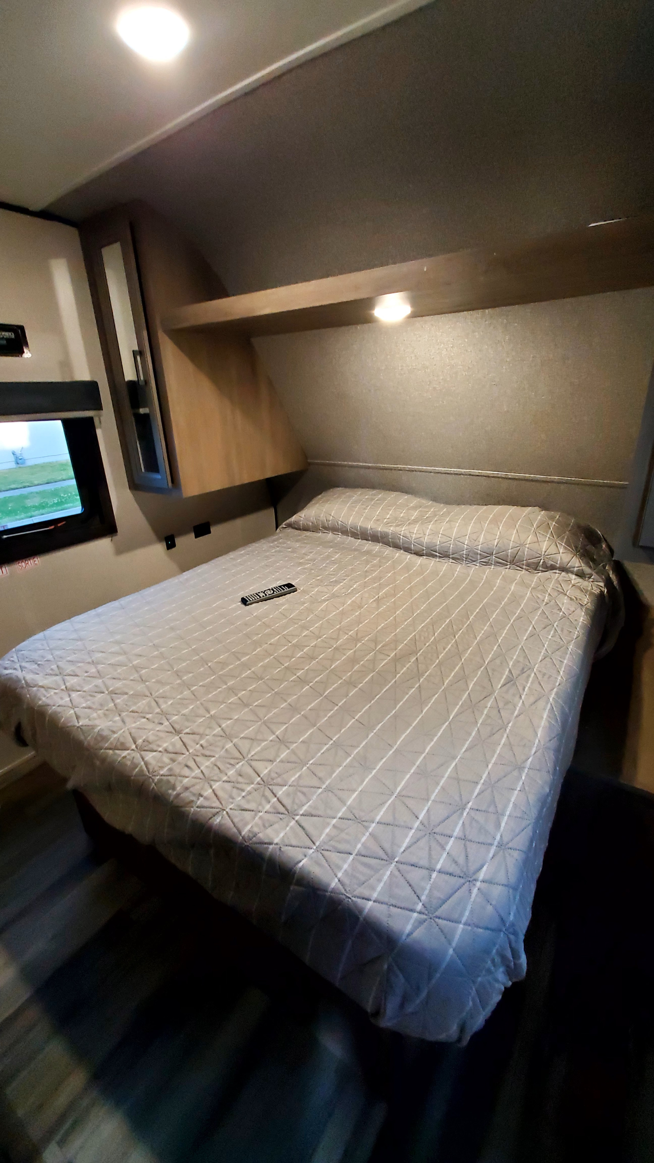 Cozy RV rental bedroom featuring a comfy bed with quilted cover, overhead storage, and a window for natural light.. Starcraft Autumn Ridge 2022