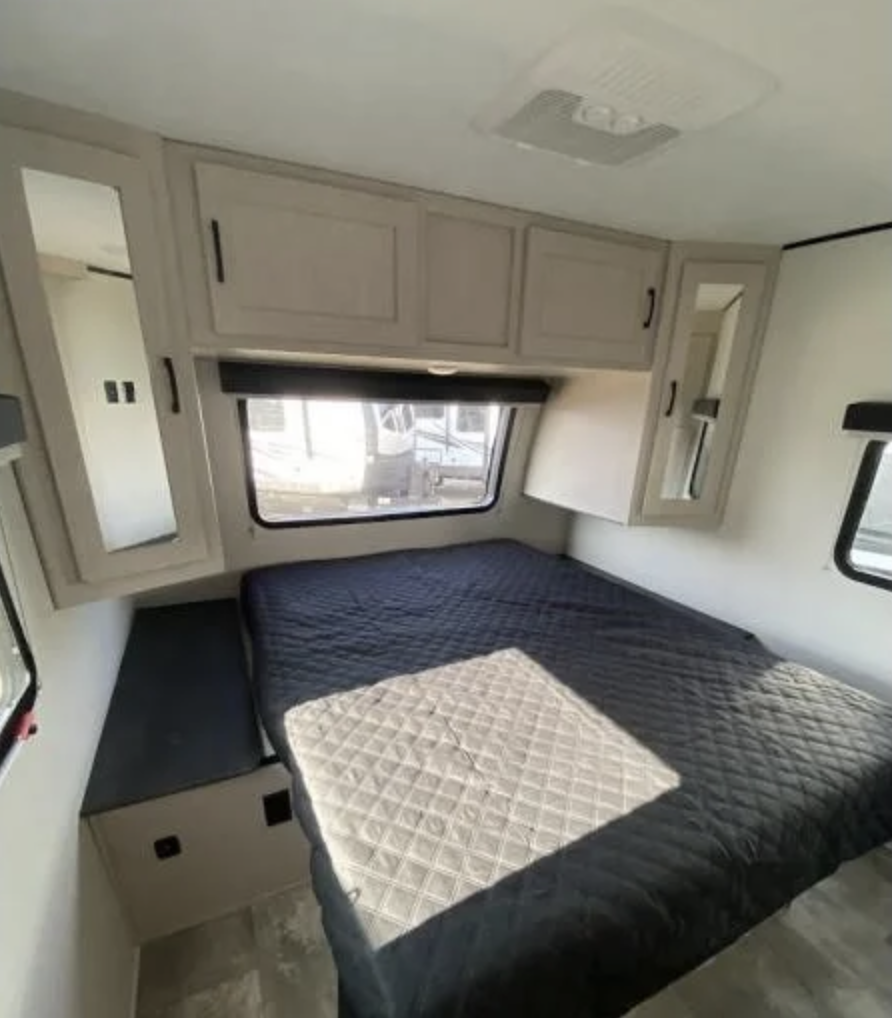 Spacious RV rental bedroom featuring a bed, overhead cabinets, windows, and an AC unit.. Coachmen Other 2022