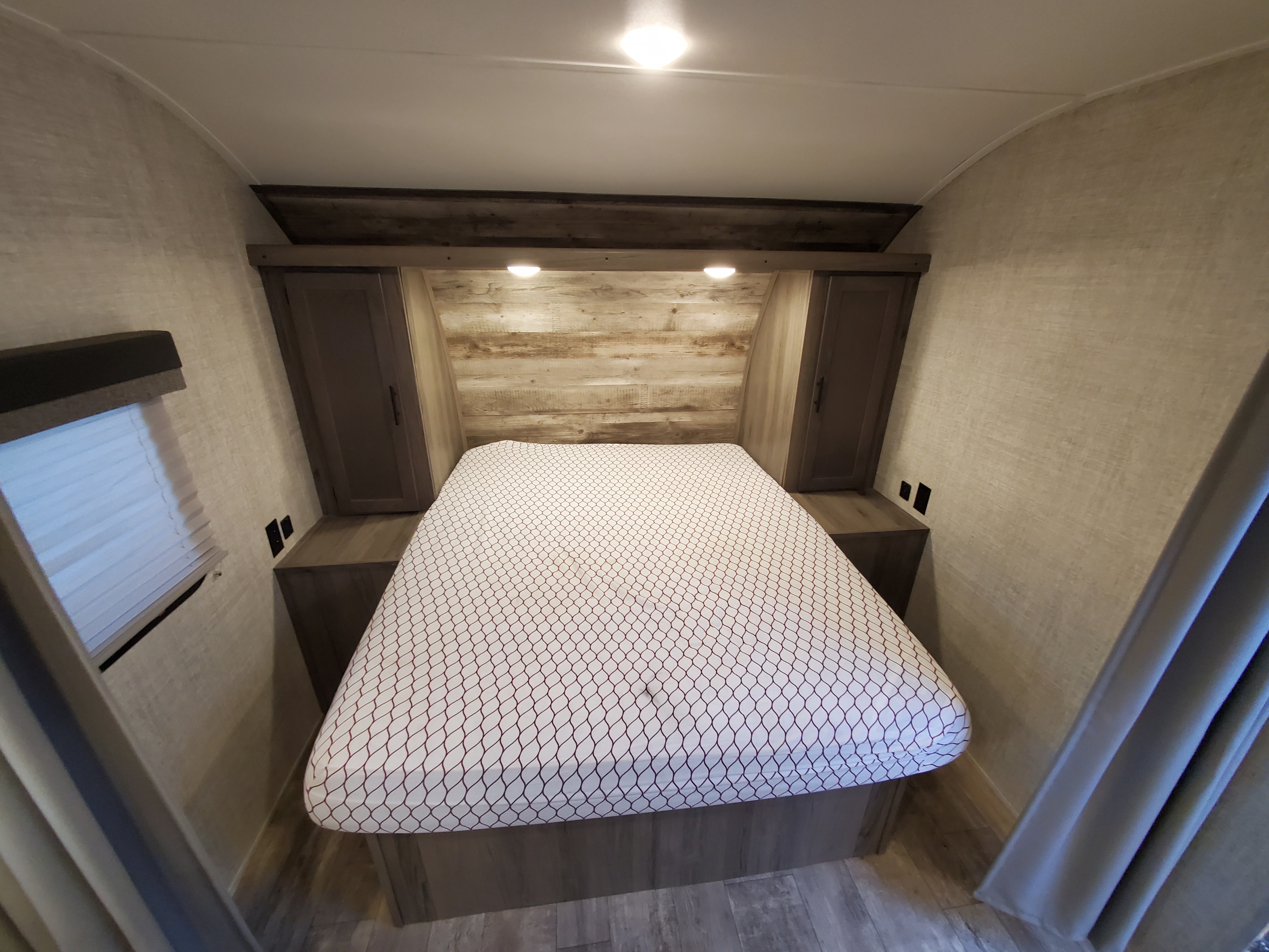 Inside a cozy RV rental bedroom: bed with patterned sheet, built-in storage, window, and warm overhead lighting.. Gulf Stream kingsport 2021