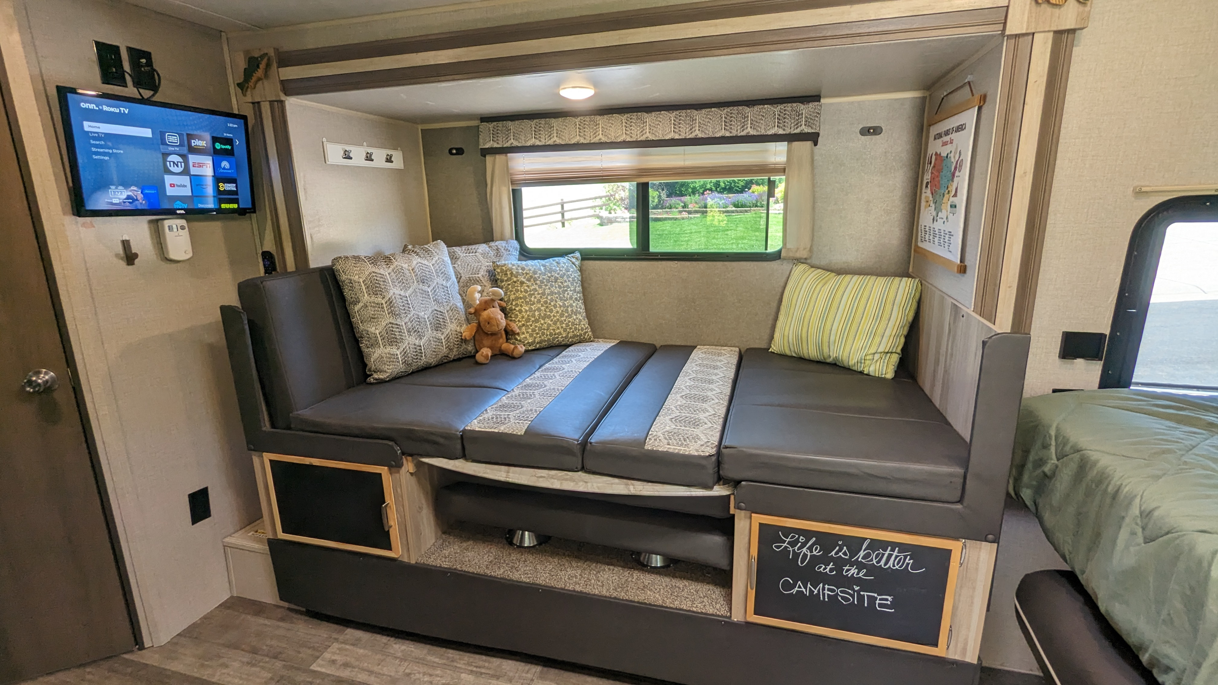 Cozy RV rental interior featuring a convertible dinette/bed, wall-mounted TV, and a 'Life is better at the CAMPSITE' sign.. Forest River Other 2021