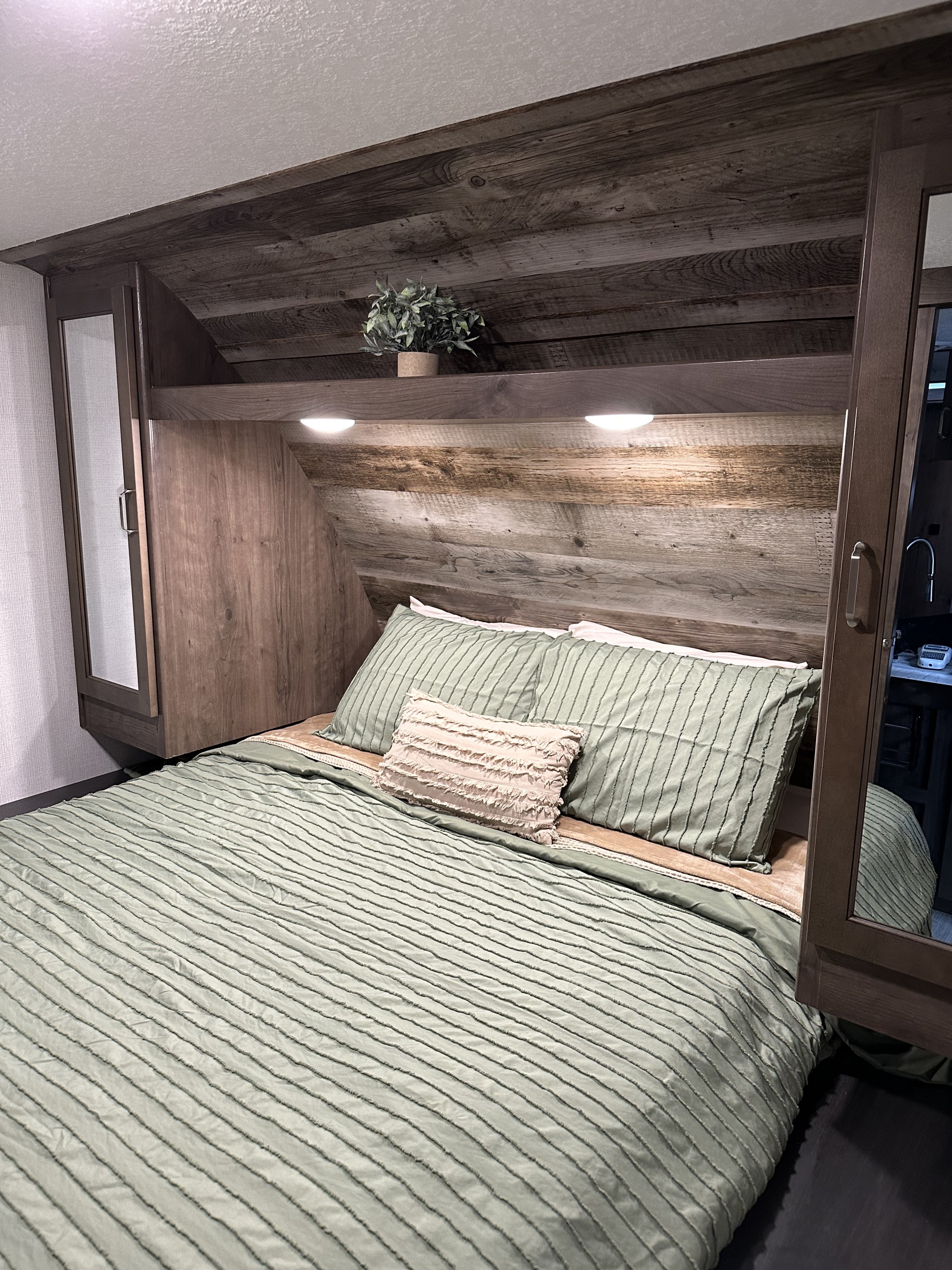 Modern RV rental bedroom featuring wood paneling, soft green bedding, built-in storage, and ambient lighting.. Keystone RV Passport SL 2021