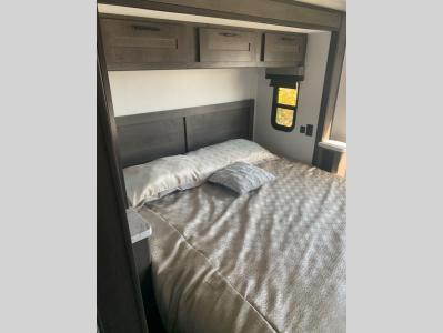 An inviting RV rental bedroom with a comfortable bed, overhead storage, and a small window.. Forest River FR3 30DS 2023