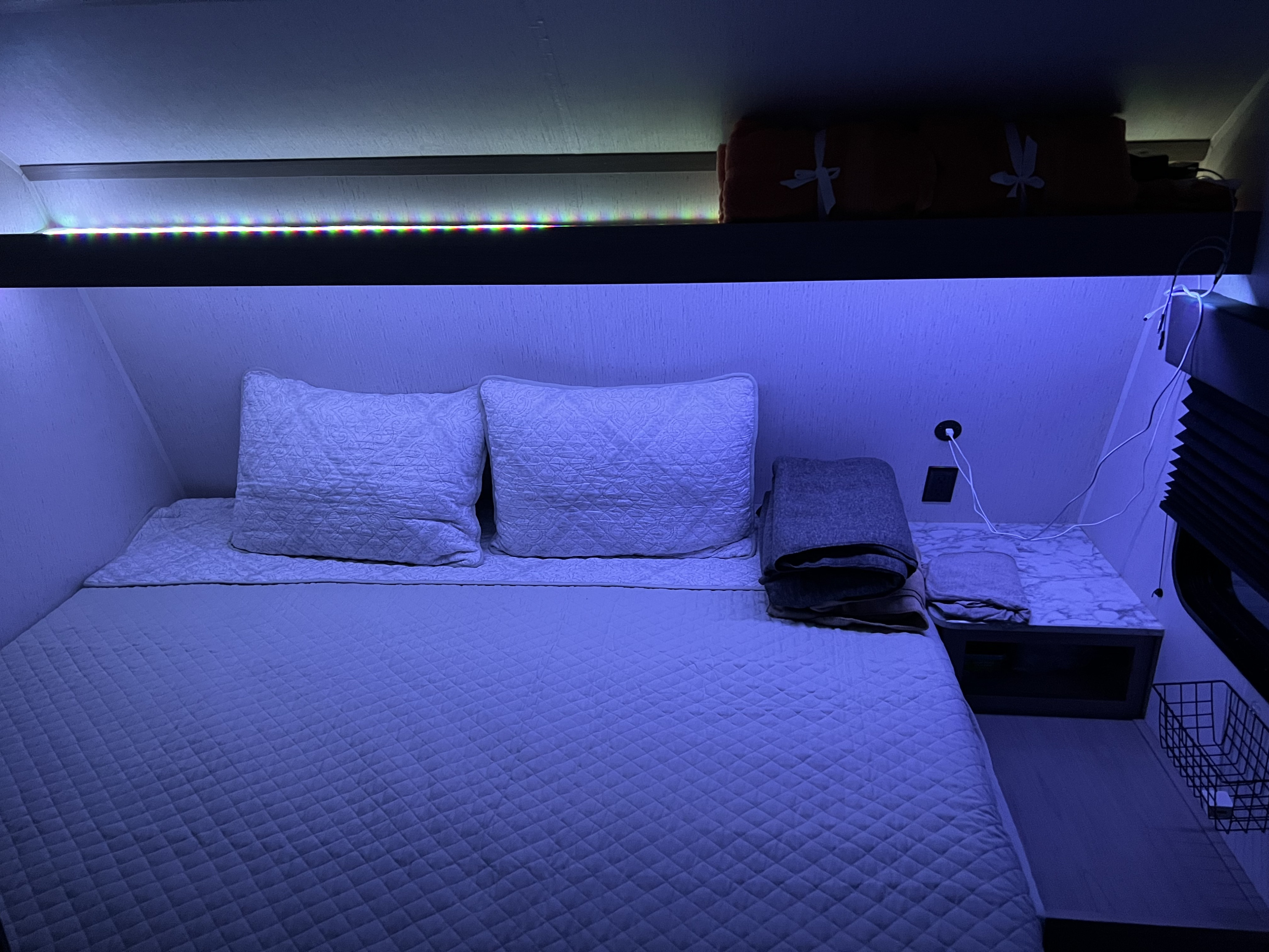 Cozy RV rental bedroom: quilted bed, purple LED lights, overhead shelf, and nightstand in a compact space.. Dutchmen Coleman Lantern LT 2022