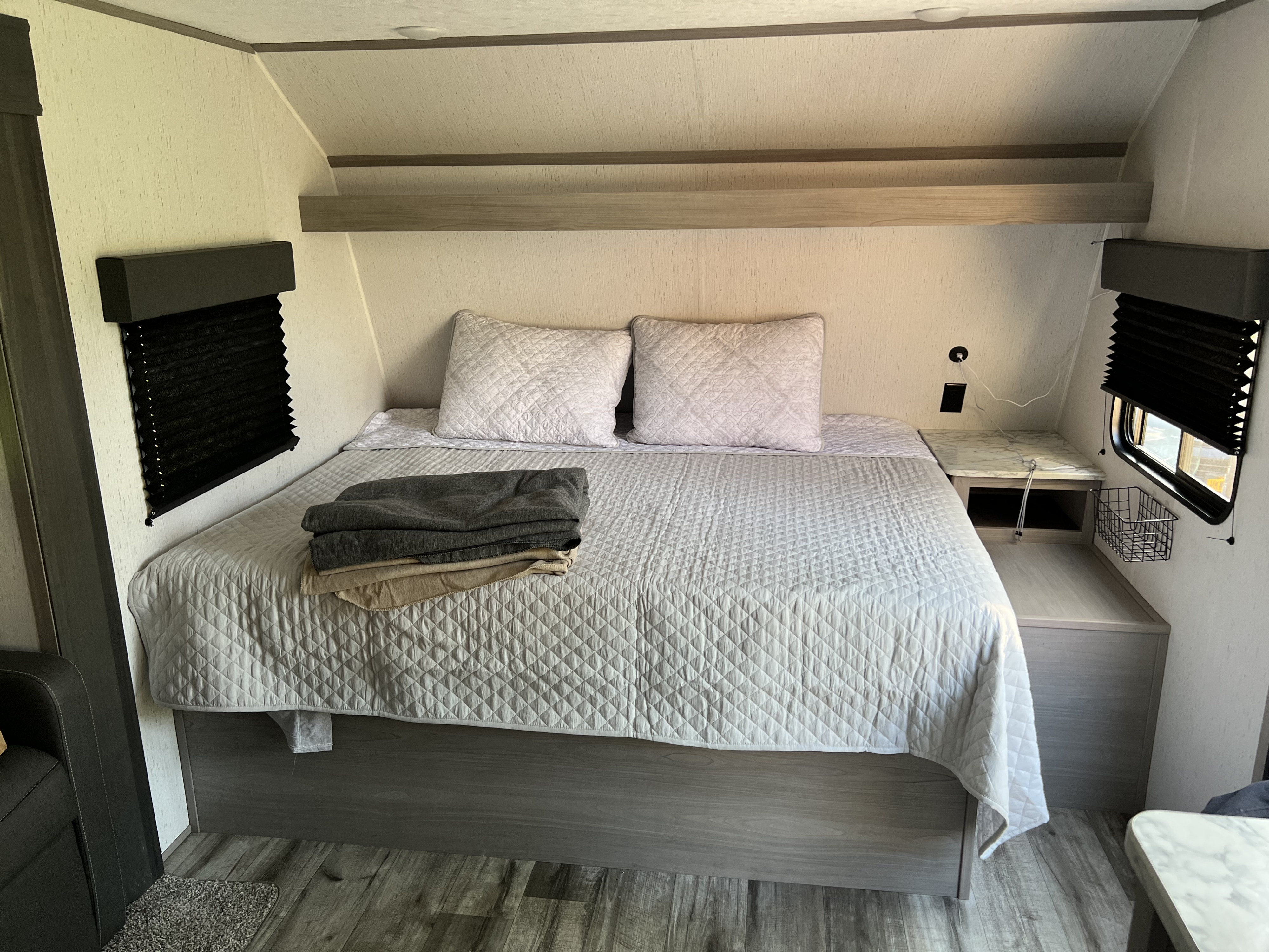 Inside an RV rental, a compact and comfortable bedroom features a quilted bed, side tables, and practical storage solutions.. Dutchmen Coleman Lantern LT 2022