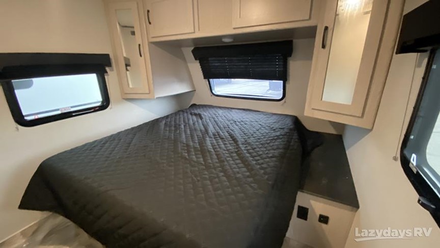 Inside an RV rental, a compact bedroom features a dark quilted bed, side windows, and ample overhead storage cabinets.. Forest River Coachmen Apex 256BHS 2022