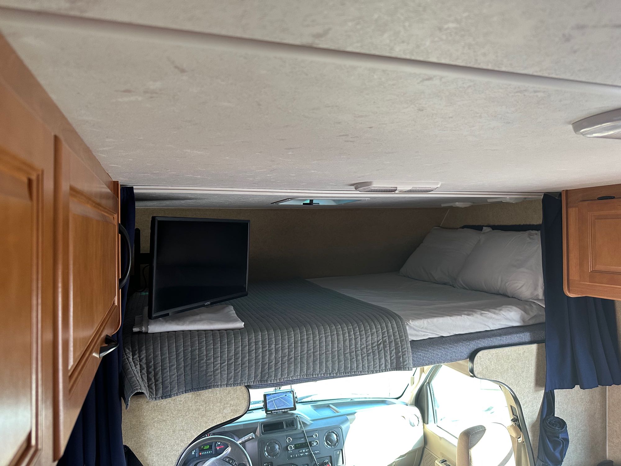 Inside an RV rental: a cozy cab-over bunk bed with a TV, pillows, and quilt, offering a comfy sleeping space above the driver's cabin.. Thor Majestic 2015