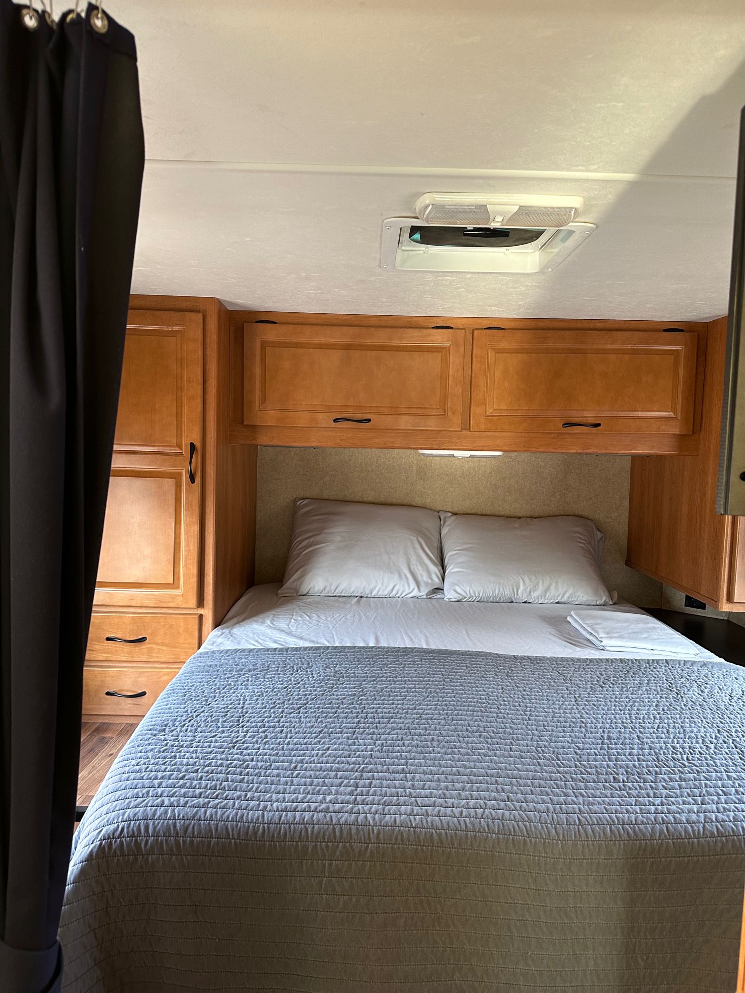 This RV rental shows a full bed with gray quilt, white pillows, wood storage cabinets, and a ceiling vent.. Thor Majestic 2015
