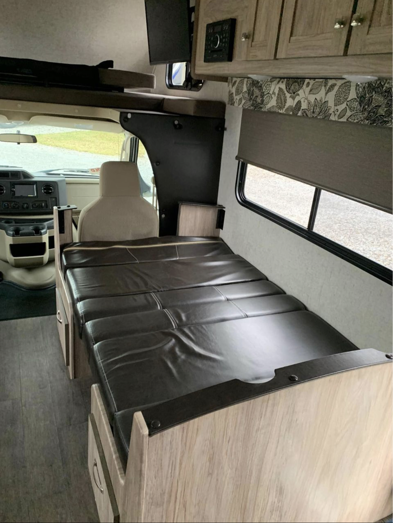RV rental interior view: large convertible bed with dark cushions, light wood cabinets, and front driving area.. Forester LE 2018