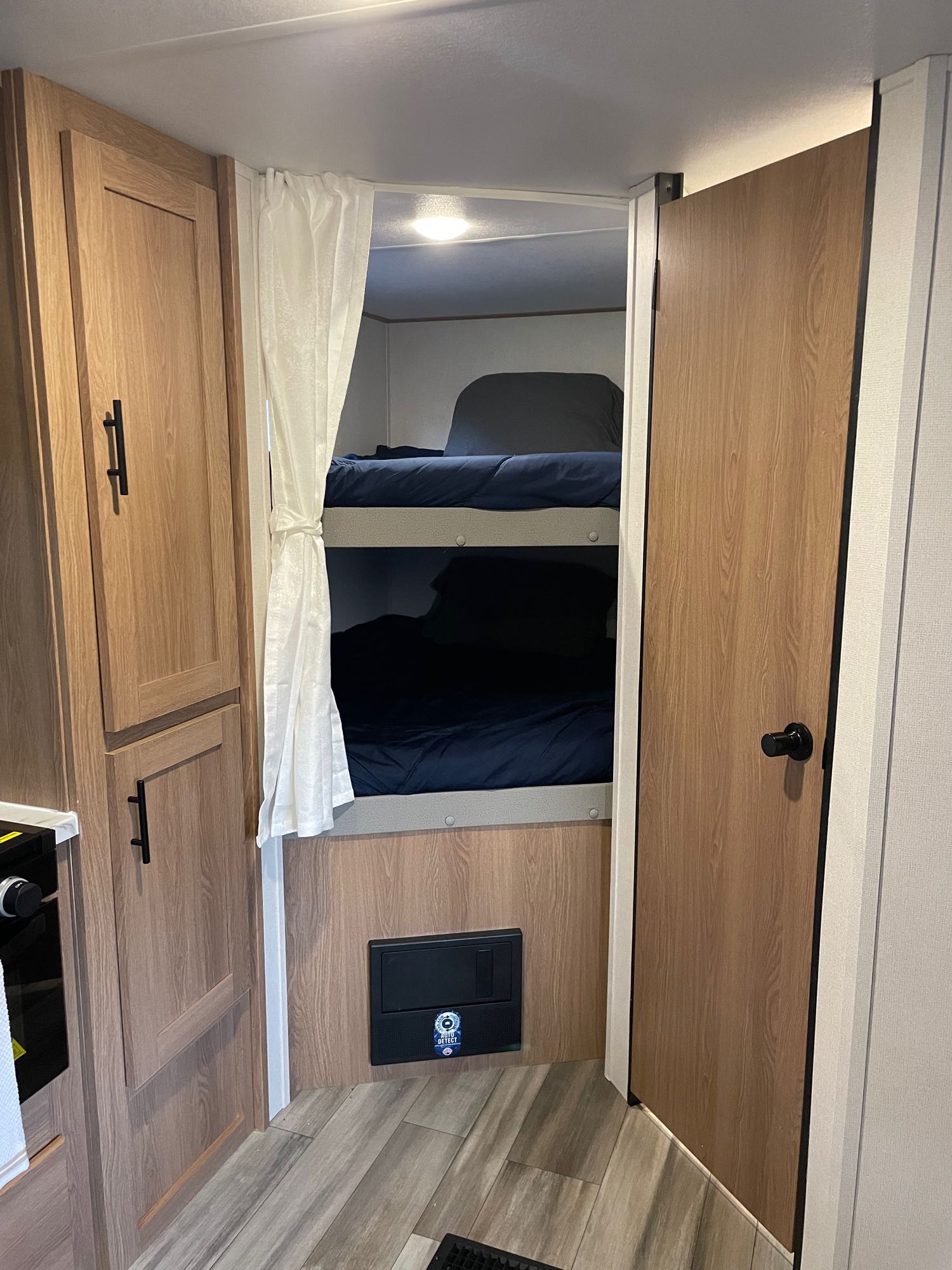RV rental interior: Bunk beds with navy bedding, storage cabinet, and door visible. White curtain adds privacy to bunks.. Forest River Prime time Avenger 2023