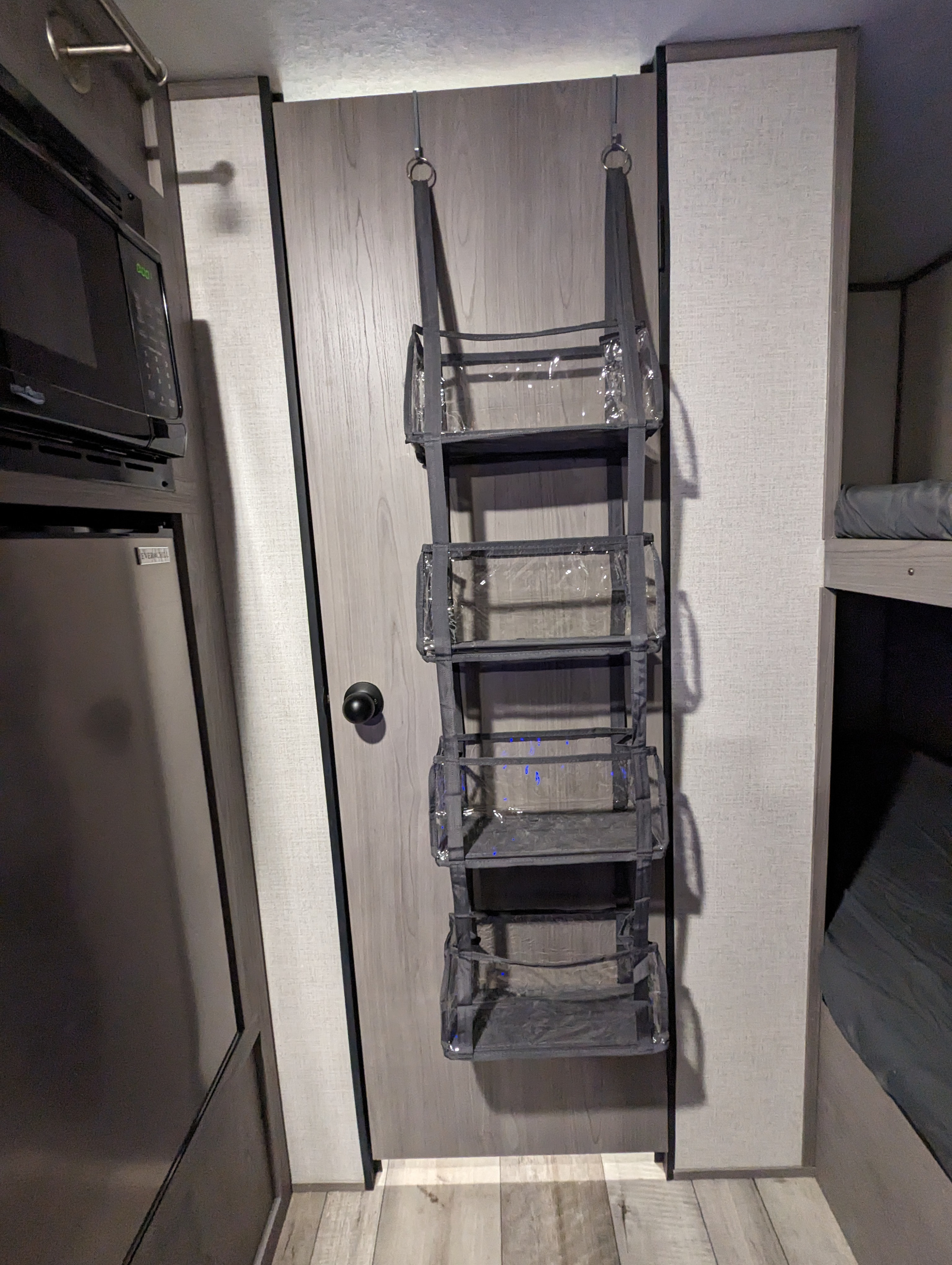RV rental interior featuring a multi-pocket clear hanging organizer on a door, next to a microwave and bunk beds.. Dutchmen Coleman Lantern LT 2023