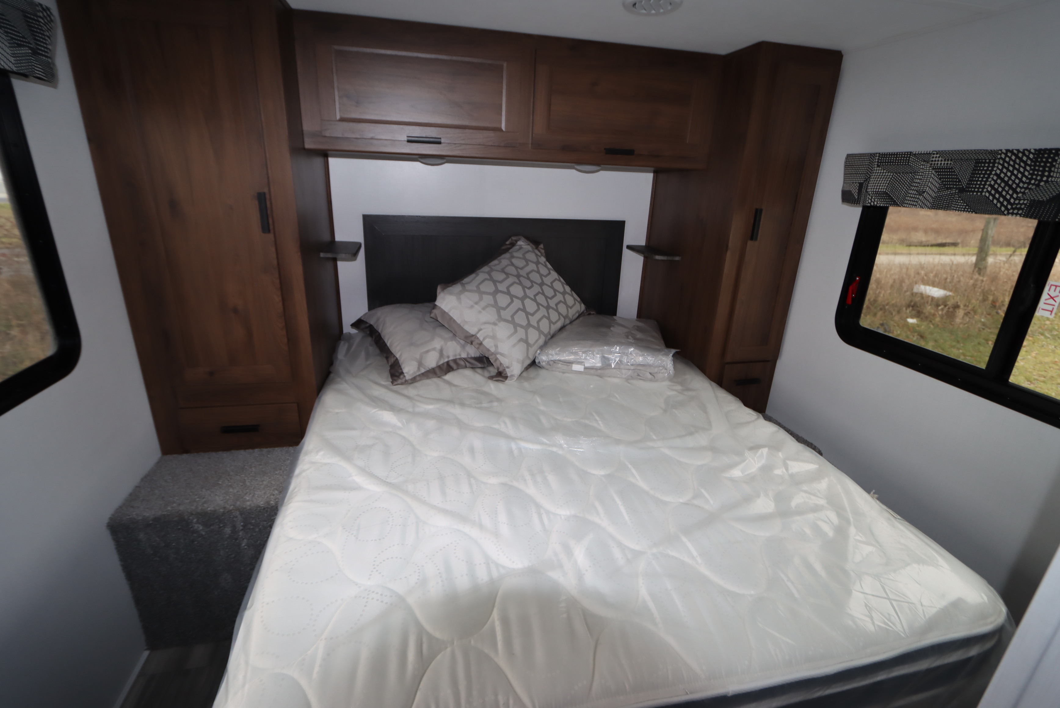 Inside an RV rental: a cozy bedroom featuring a new mattress, headboard, overhead storage, and side windows.. Forest River Sunseeker LE 2022