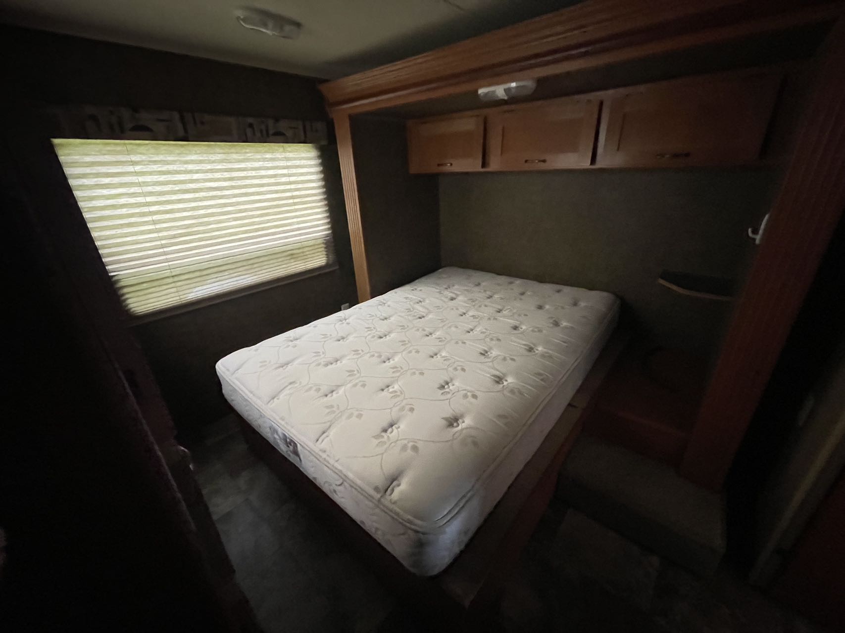 Compact RV rental bedroom with a white mattress, overhead wooden cabinets, and window with closed blinds. Functional interior.. Forest River Cherokee Grey Wolf 2015