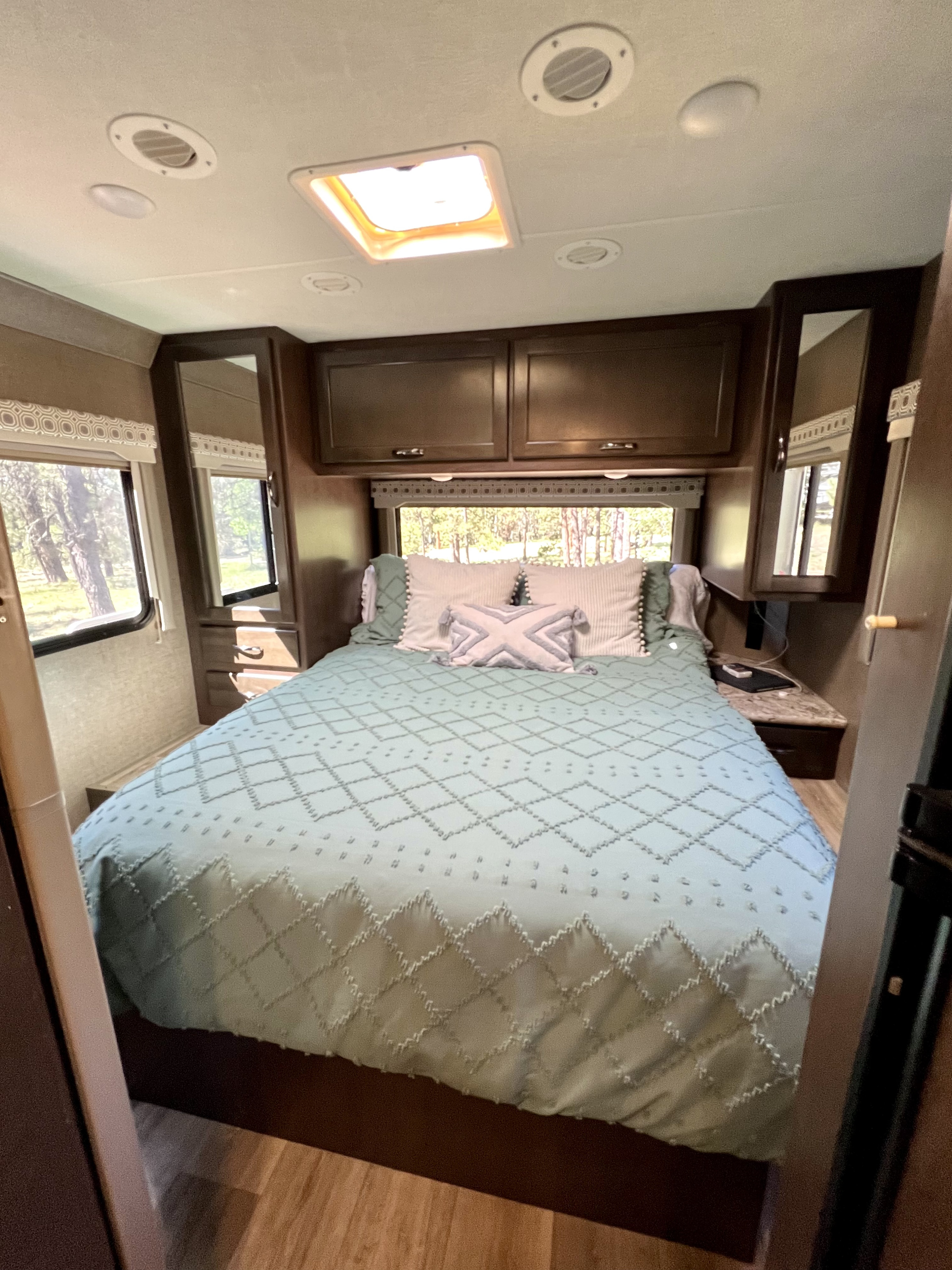 Comfortable RV rental bedroom featuring a full bed, overhead storage, and natural light from outside windows.. Thor Four Winds 2020