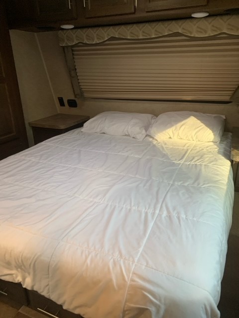 Inside a clean RV rental: a neatly made bedroom with white bedding, pillows, and window blinds for comfort.. Forest River Flagstaff Super Lite 2016