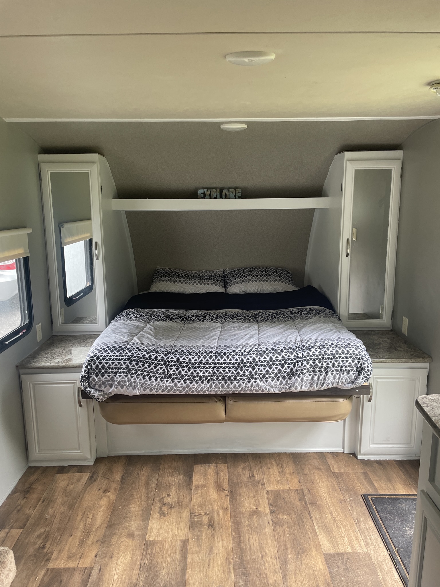 Cozy RV rental bedroom: a bed with geometric bedding, mirrored side cabinets, and wood-look flooring. Ready for travel!. Forest River Wildwood X-Lite 2016