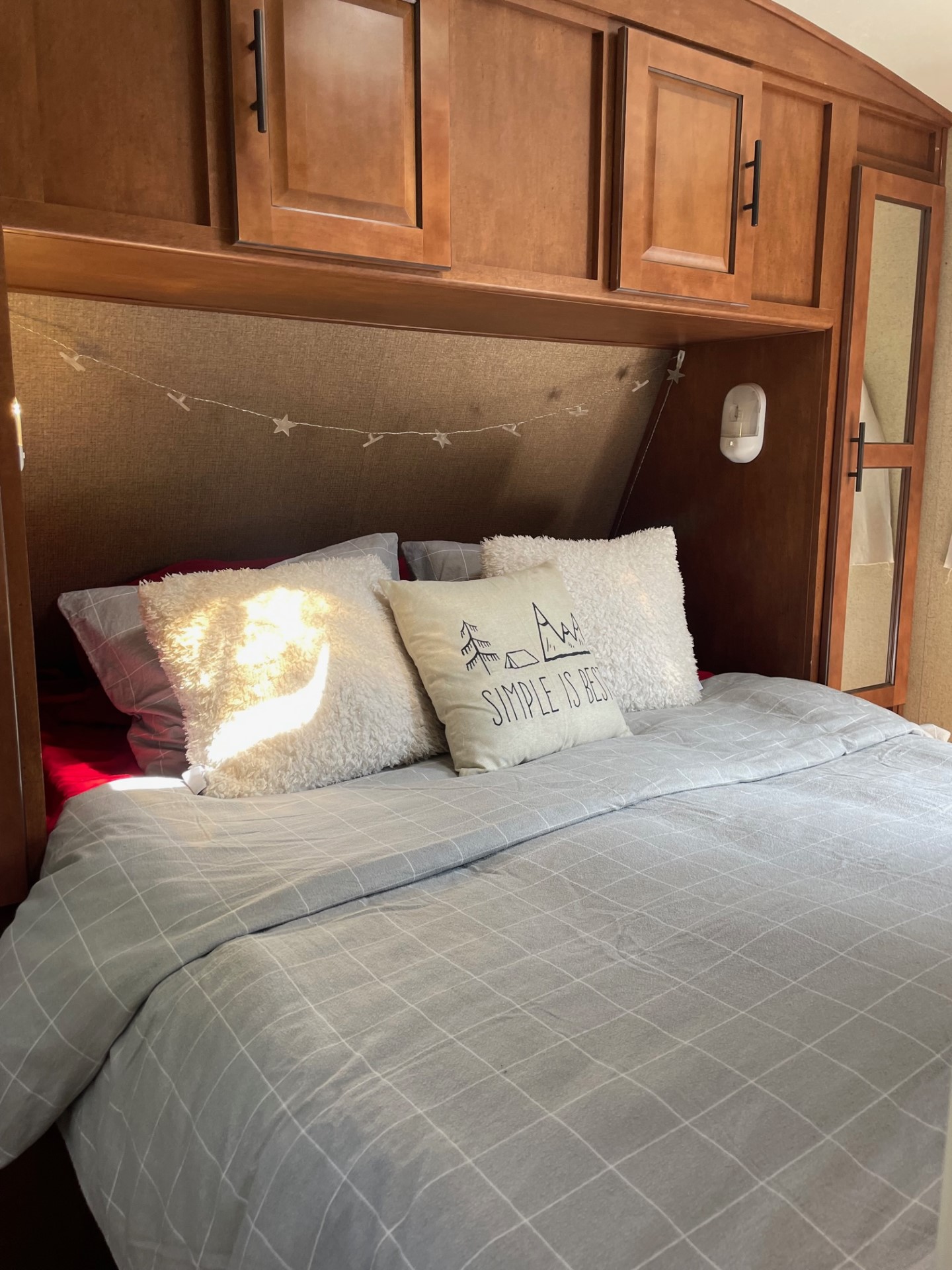Inside a comfortable RV rental bedroom featuring a grey grid duvet, decorative pillows, and overhead cabinets.. Forest River Surveyor 2014